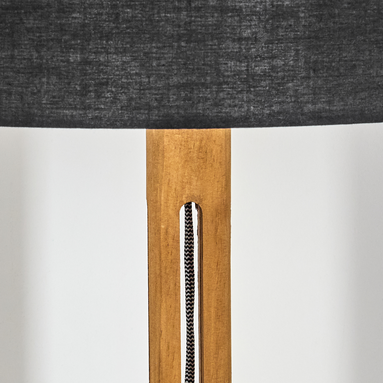 Nahaufnahme einer Lampe. Ein dunkelgrauer Lampenschirm sitzt auf einem Holzrahmen. Ein schwarz-weißes Kabel verläuft am Rahmen entlang.