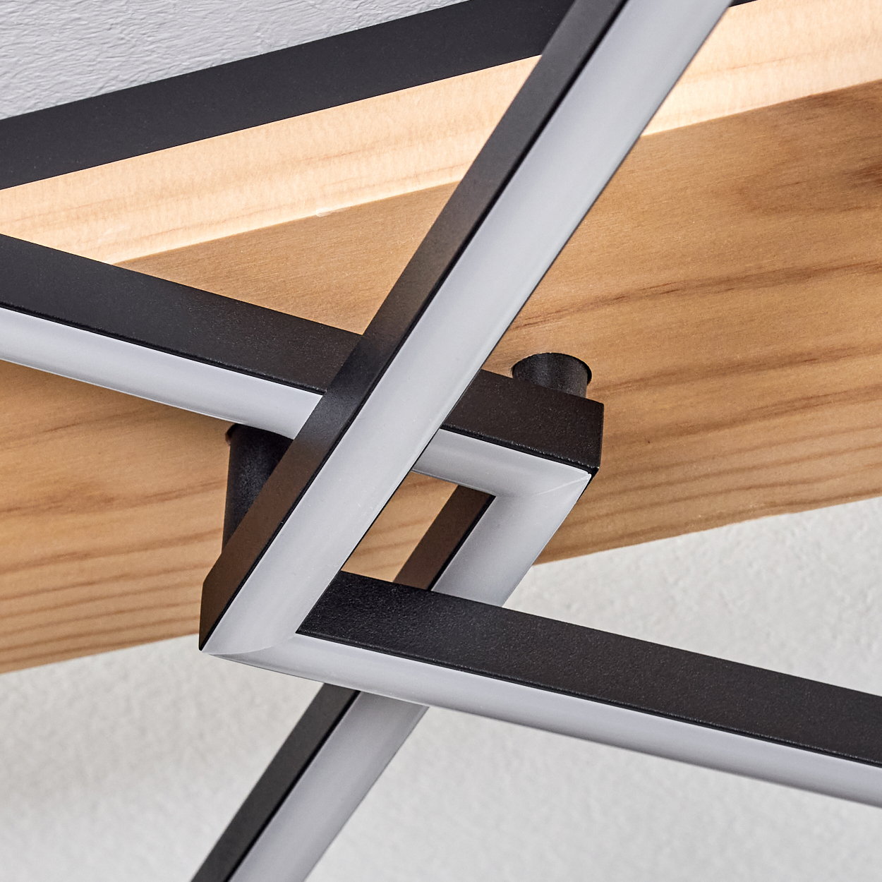 Nahaufnahme einer modernen Leuchte. Sie hat schwarze Metallrahmen mit weißen LED-Streifen vor Holz und weißer Wand.