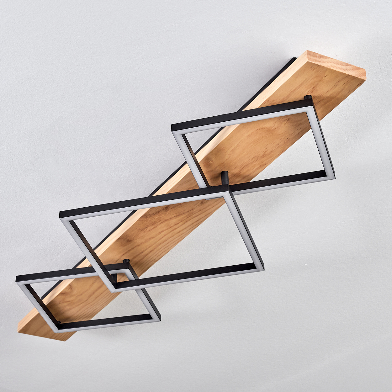 Deckenleuchte mit Holzbalken und schwarzen, geometrischen Lichtrahmen vor weißer Decke.