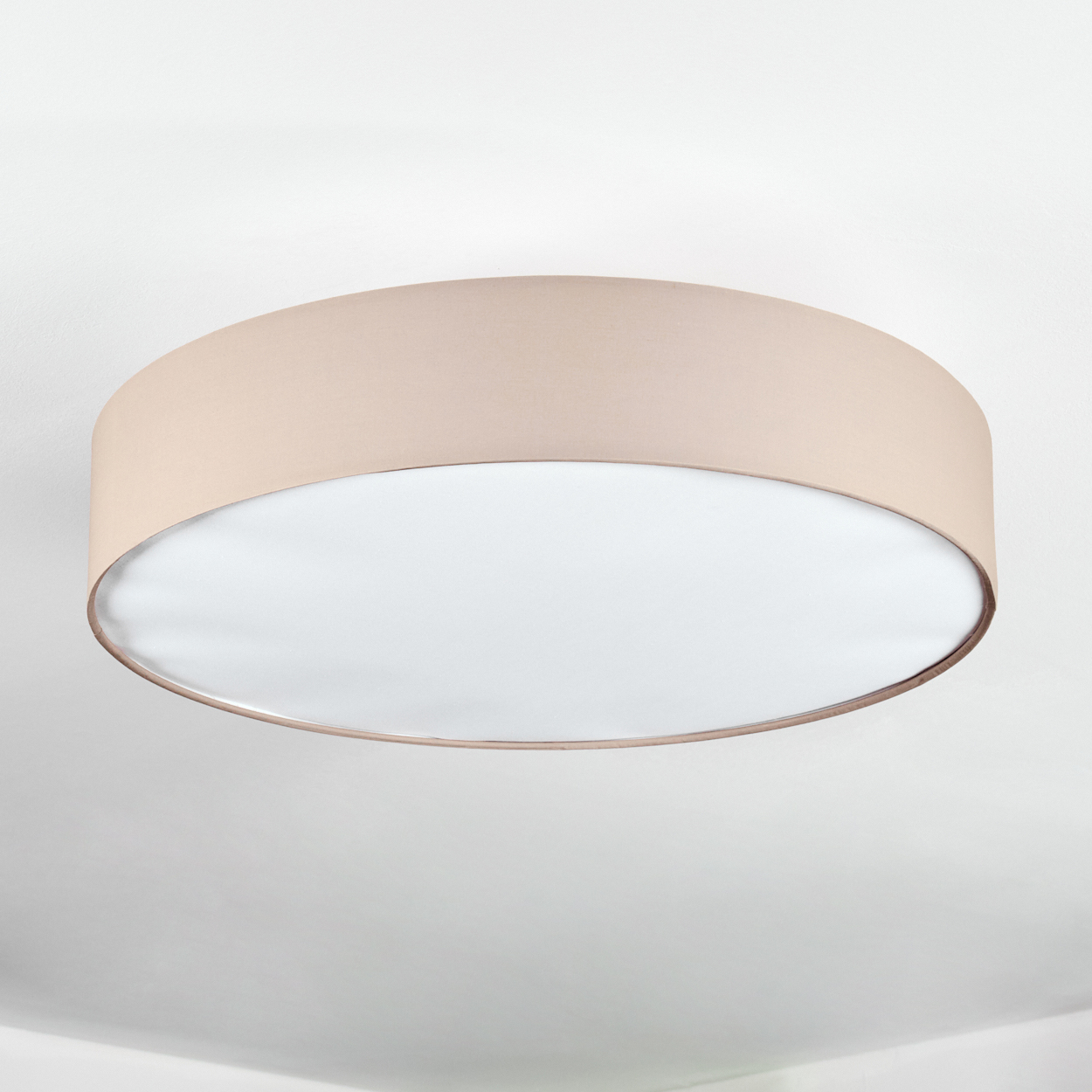 Eine beige kreisförmige Deckenleuchte. Sie hat einen beigefarbenen Schirm und eine weiße, diffuse Lichtfläche. Der Hintergrund ist eine weiße Decke.