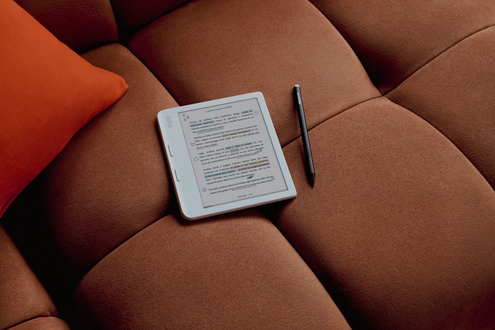 Czytnik e-booków z rysikiem spoczywa na brązowej kanapie, z pomarańczową poduszką w tle. Ekran wyświetla tekst.