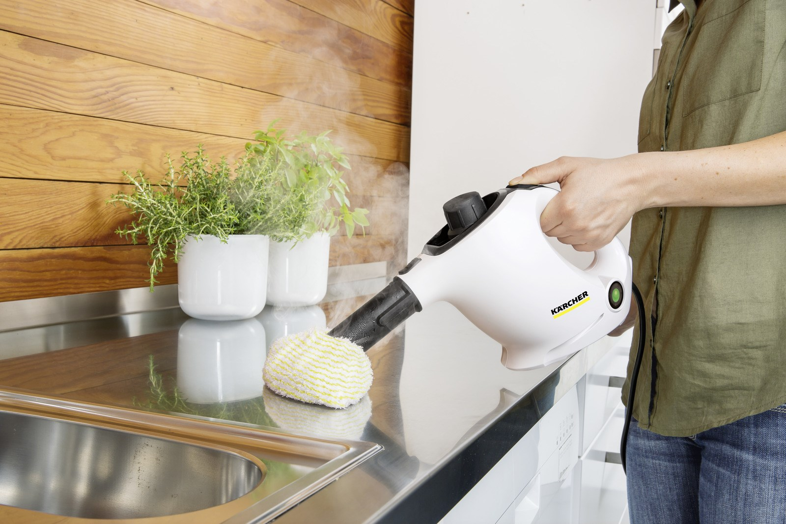 Osoba używa białego parownika na powierzchni ze stali nierdzewnej. Rośliny w białych donicach obok, para unosi się.