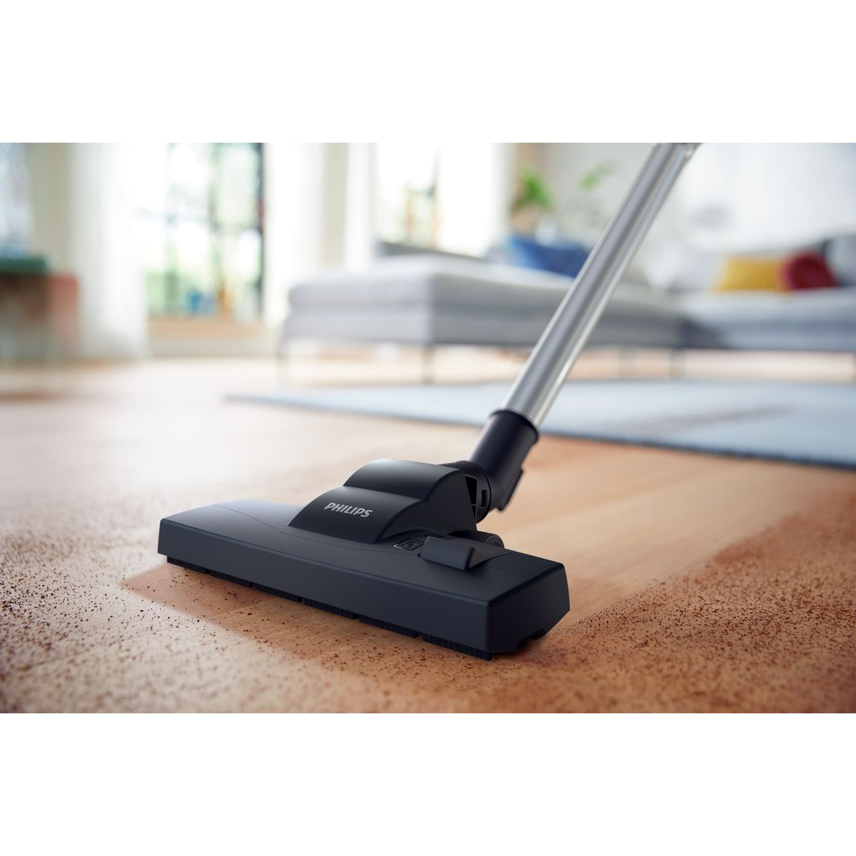 Ein Philips-Staubsaugerkopf liegt auf einem Holzboden. Im Hintergrund ist ein Wohnzimmer mit Sofa und Teppich zu sehen.