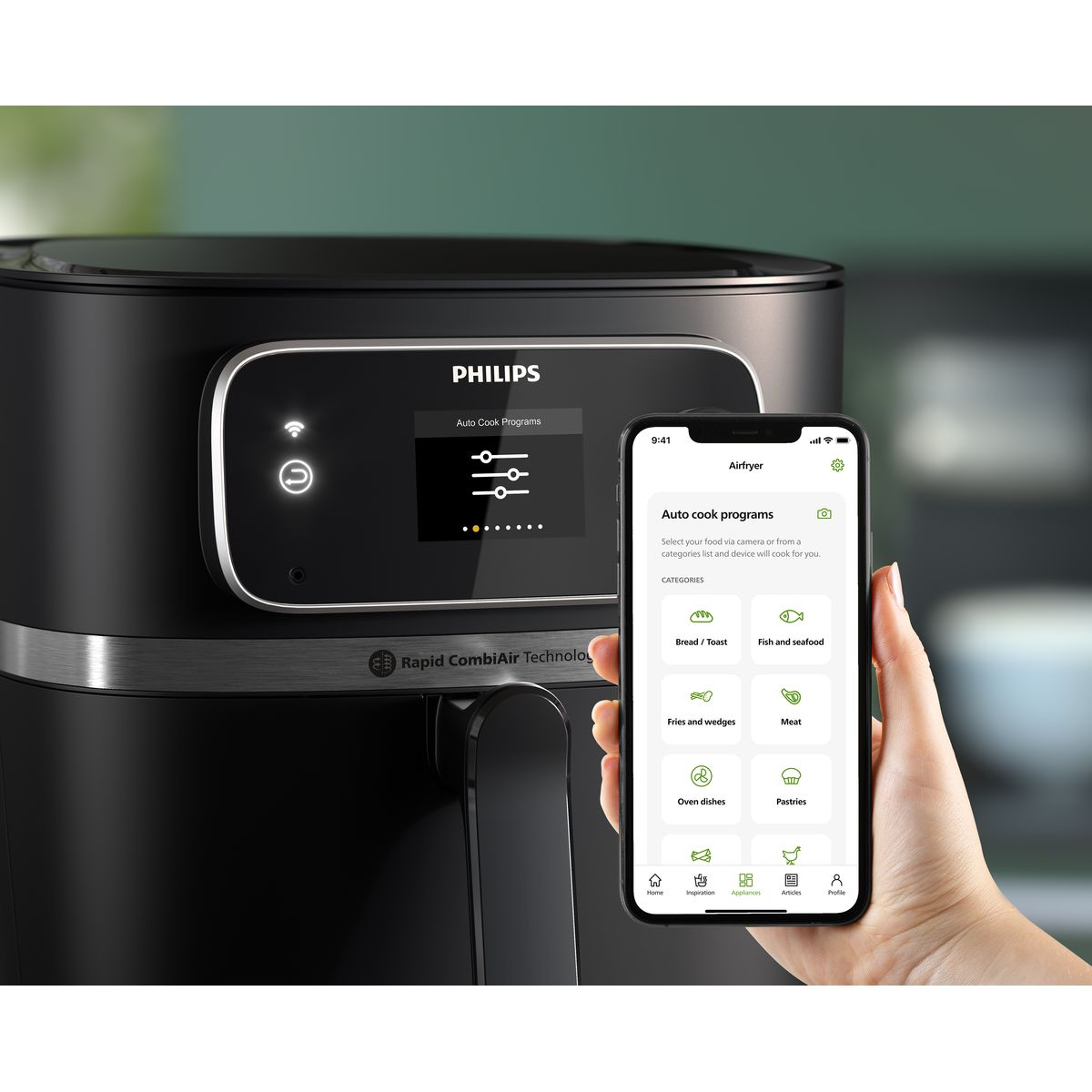 Ein Philips-Heißluftfritteuse mit einem Smartphone, das Kochprogramme anzeigt. Eine Hand hält das Telefon. Die Heißluftfritteuse ist schwarz.