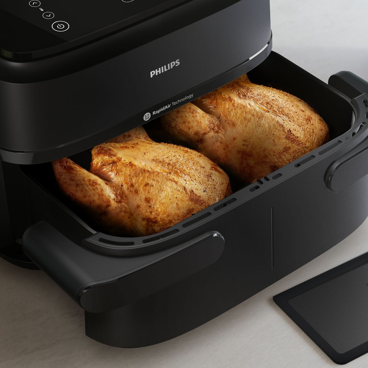 Una friggitrice ad aria con due polli arrosto all'interno. La friggitrice è nera, con il logo Philips.