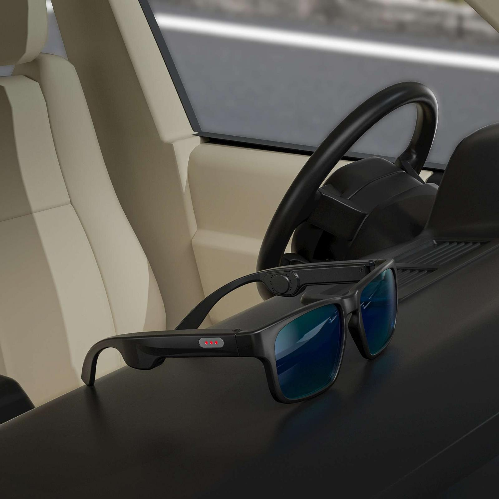 Schwarze Smartglasses auf dem Armaturenbrett eines Autos. Lenkrad, cremefarbener Sitz und Fenster im Hintergrund.