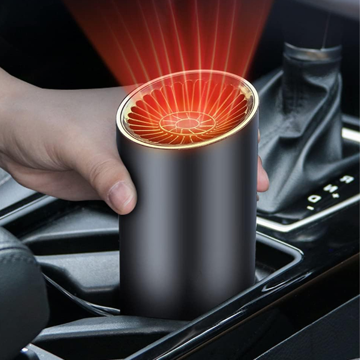 Eine Hand hält eine schwarze Autoheizung, von der rote Hitzestrahlen ausgehen. Sie befindet sich in der Konsole eines Autos, in der Nähe des Schalthebels.