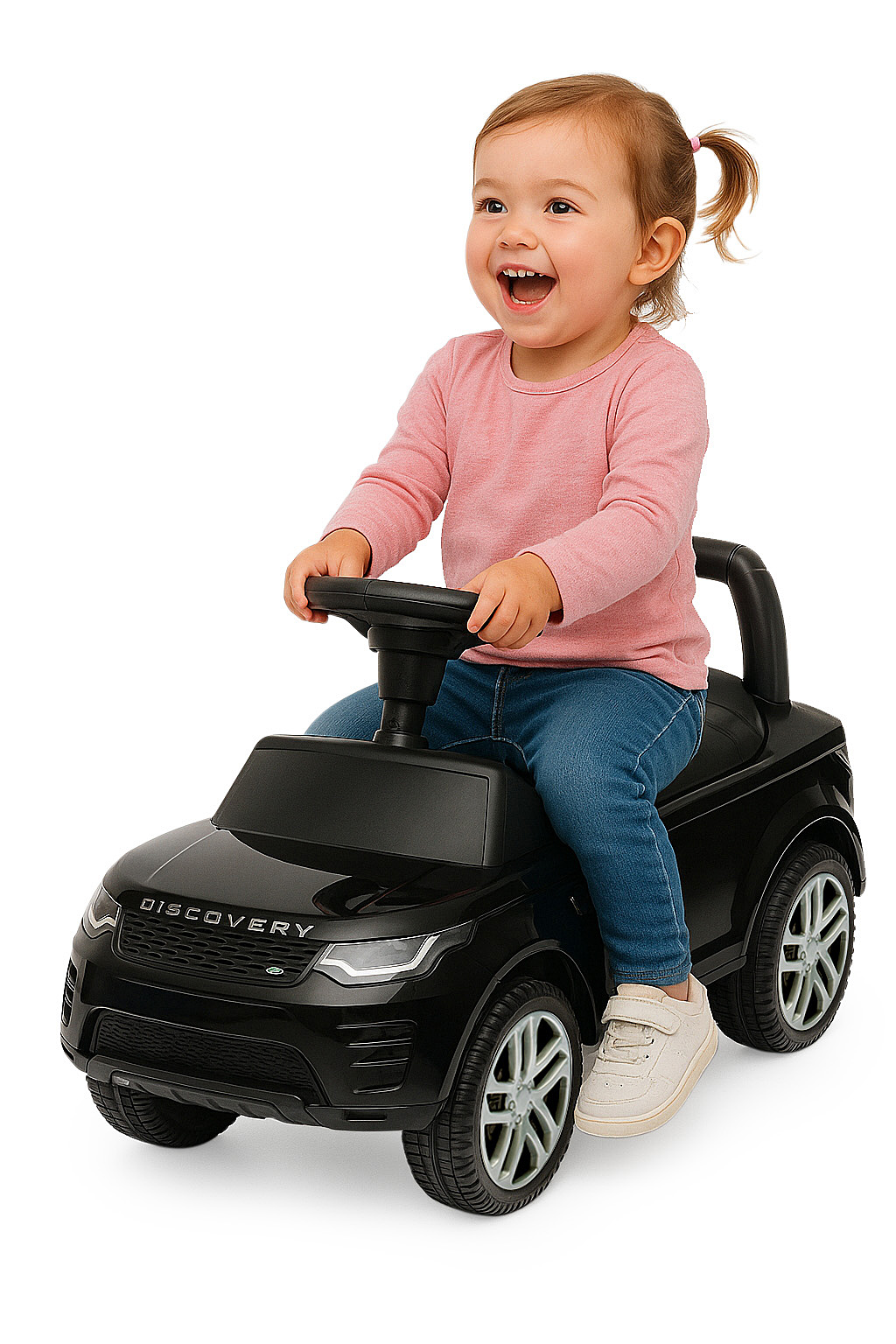 Un bambino sorridente con camicia rosa e jeans è seduto su un'auto giocattolo nera, tenendo il volante. Sfondo bianco.