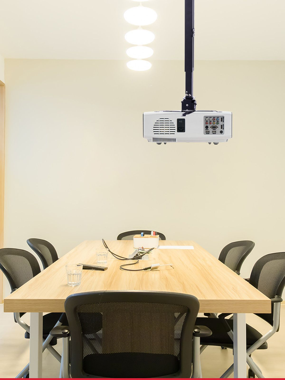 Una sala conferenze con un proiettore montato a soffitto, tavolo, sedie e luci. La stanza è ben illuminata e moderna.