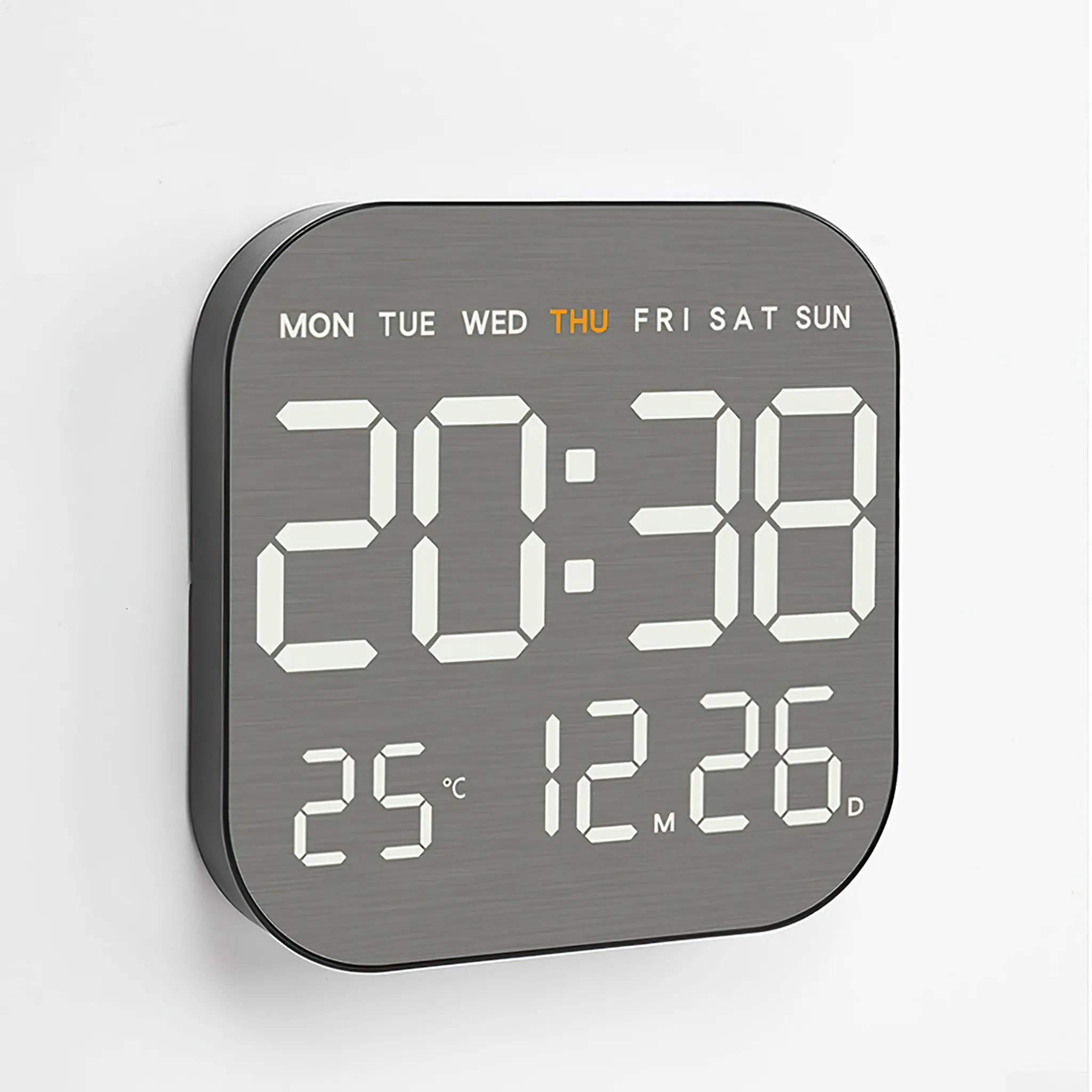 Digitaluhr, die 20:38, 25 Grad und 12.26 anzeigt. Die Wochentage stehen oben. Der Hintergrund ist eine weiße Wand.
