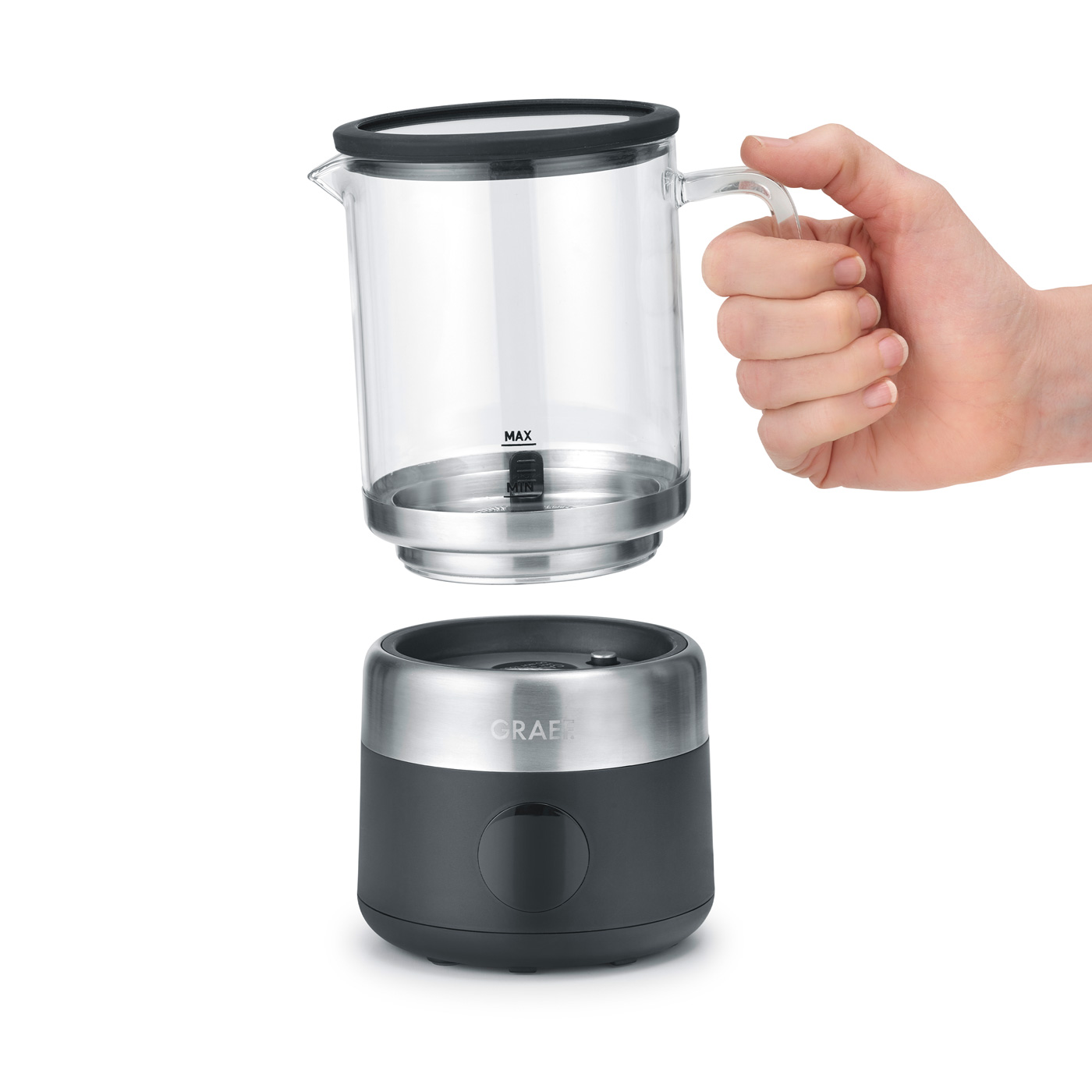 Une main tient une carafe en verre au-dessus d'une base gris foncé et argentée. La carafe a un couvercle noir et est au-dessus de la base.