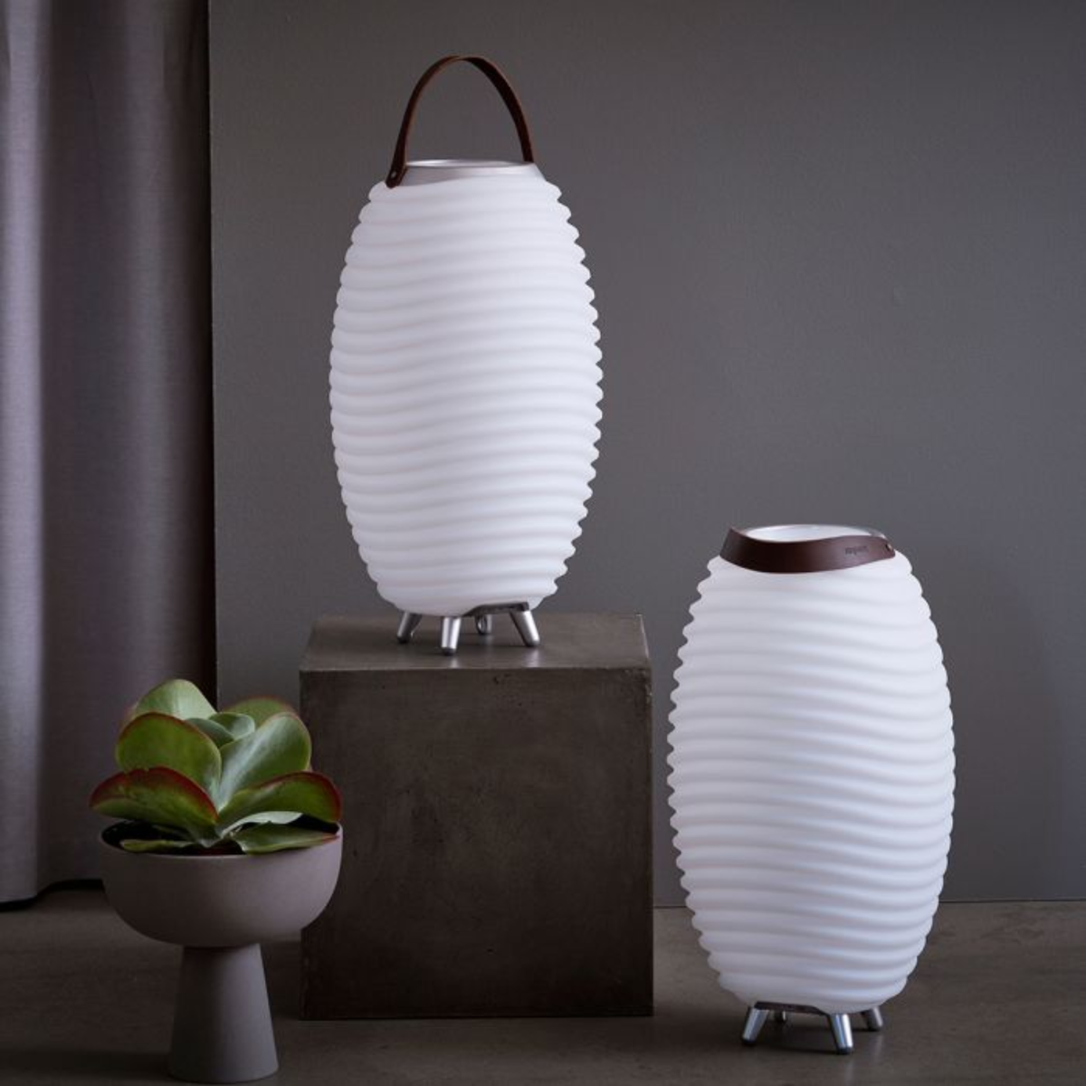 Twee witte lampen met golvende textuur, bruine handvatten en zilveren poten. Een plant in een grijze pot links.