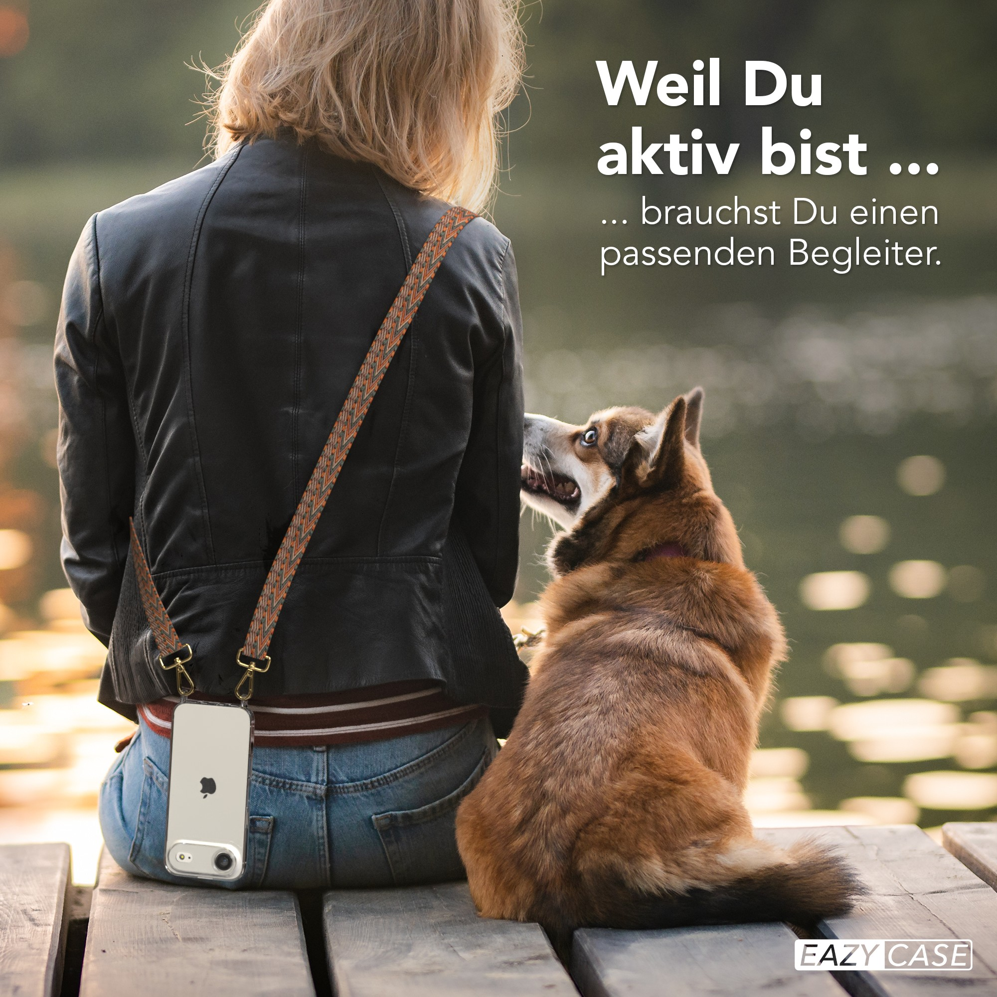 Eine Frau sitzt mit dem Rücken zur Kamera. Ein Hund schaut sie an. Ein iPhone hängt an ihrem Hals. See im Hintergrund.