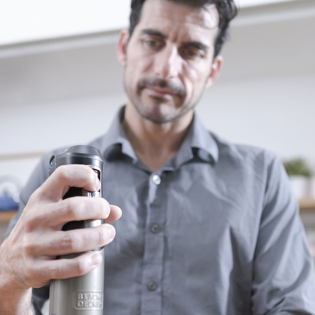 Mężczyzna w szarej koszuli trzyma urządzenie Black+Decker. Wydaje się, że patrzy na nie z neutralnym wyrazem twarzy.