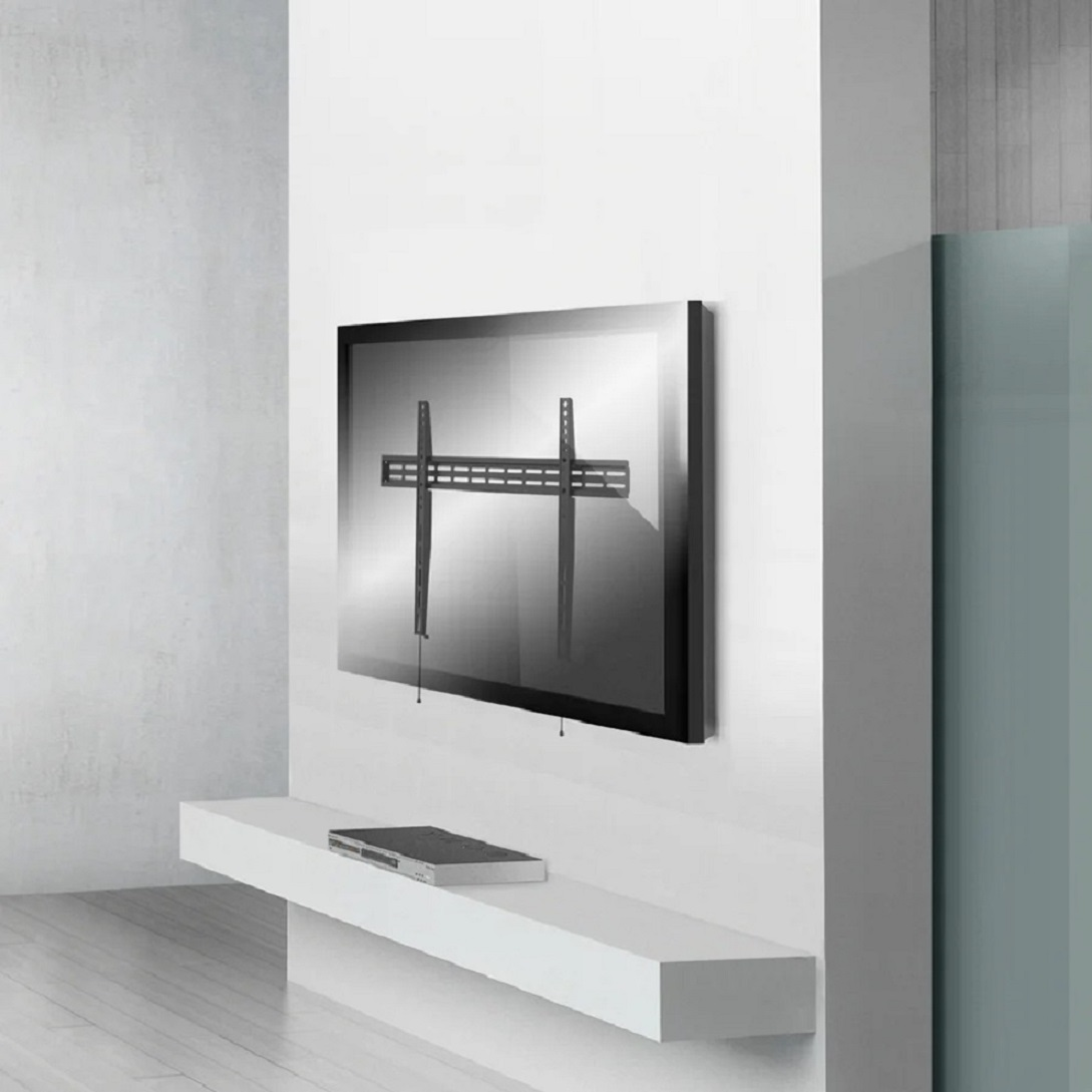 Un televisor con un soporte de montaje en una pared blanca. Una estantería blanca debajo sostiene un dispositivo. El fondo es una pared blanca y gris.