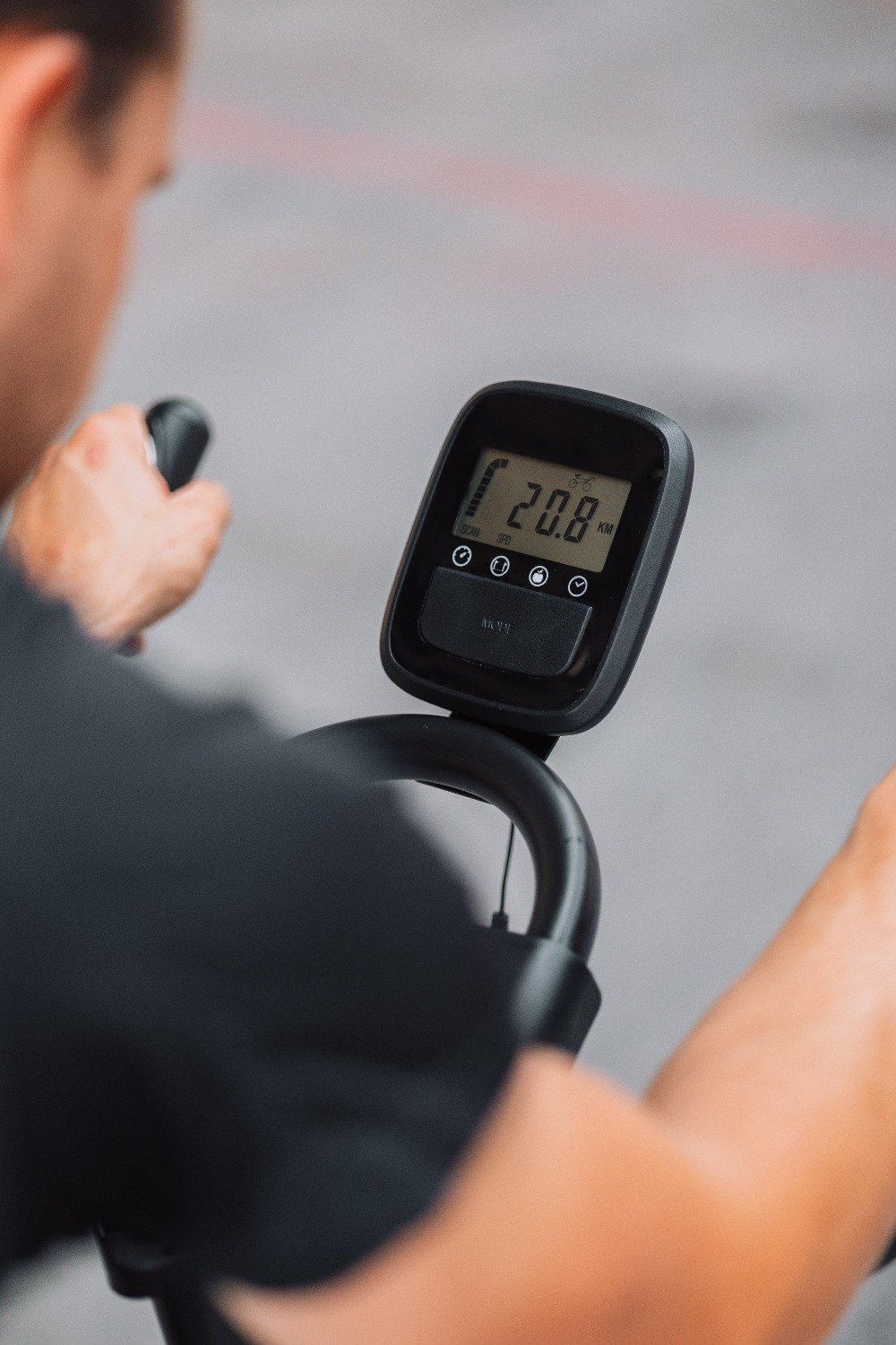 Une personne sur un vélo d'appartement, l'écran affiche 20,8 KM. Les poignées et les bras de la personne sont visibles.