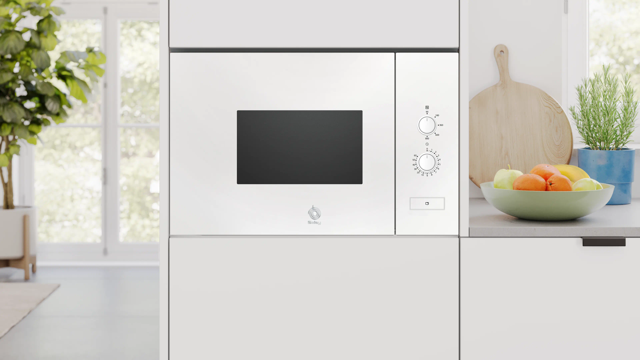 Biała kuchenka mikrofalowa do zabudowy z panelem sterowania. Na blacie stoi miska z owocami. Roślina w tle.