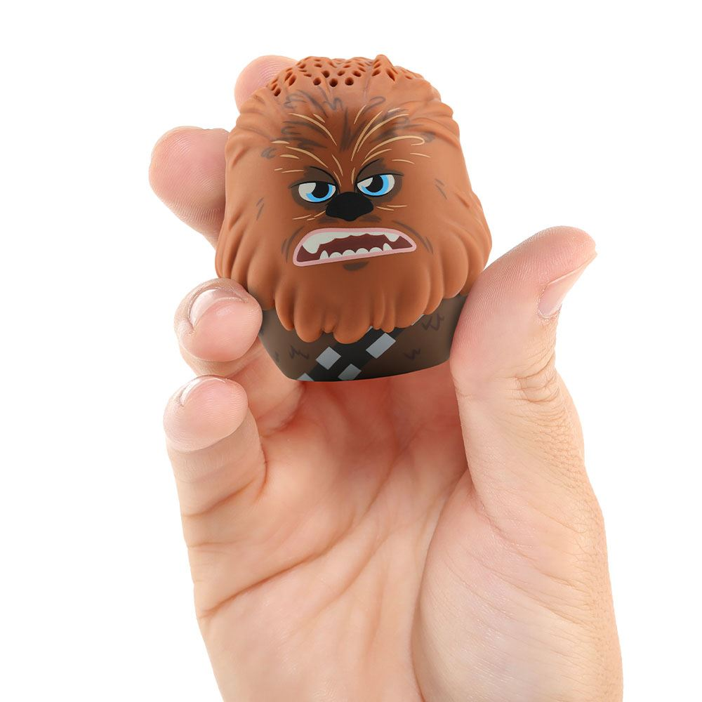 Bir el Chewbacca oyuncağını tutuyor. Kahverengi, mavi gözlü ve küçük ağızlı. Oyuncağın üstünde bir hoparlör var.