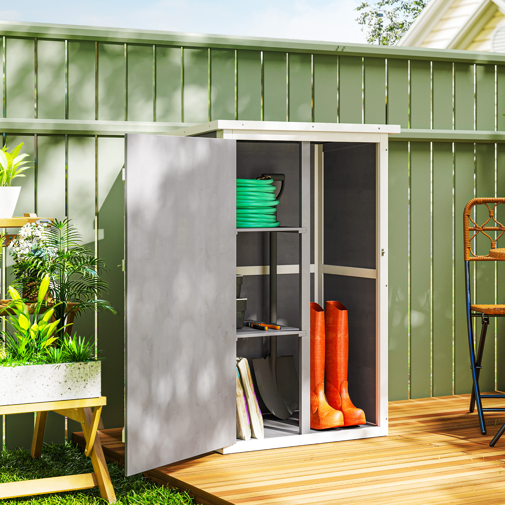 Un capanno da giardino con porta aperta. All'interno ci sono attrezzi e stivali. Una recinzione verde e piante circondano il capanno.