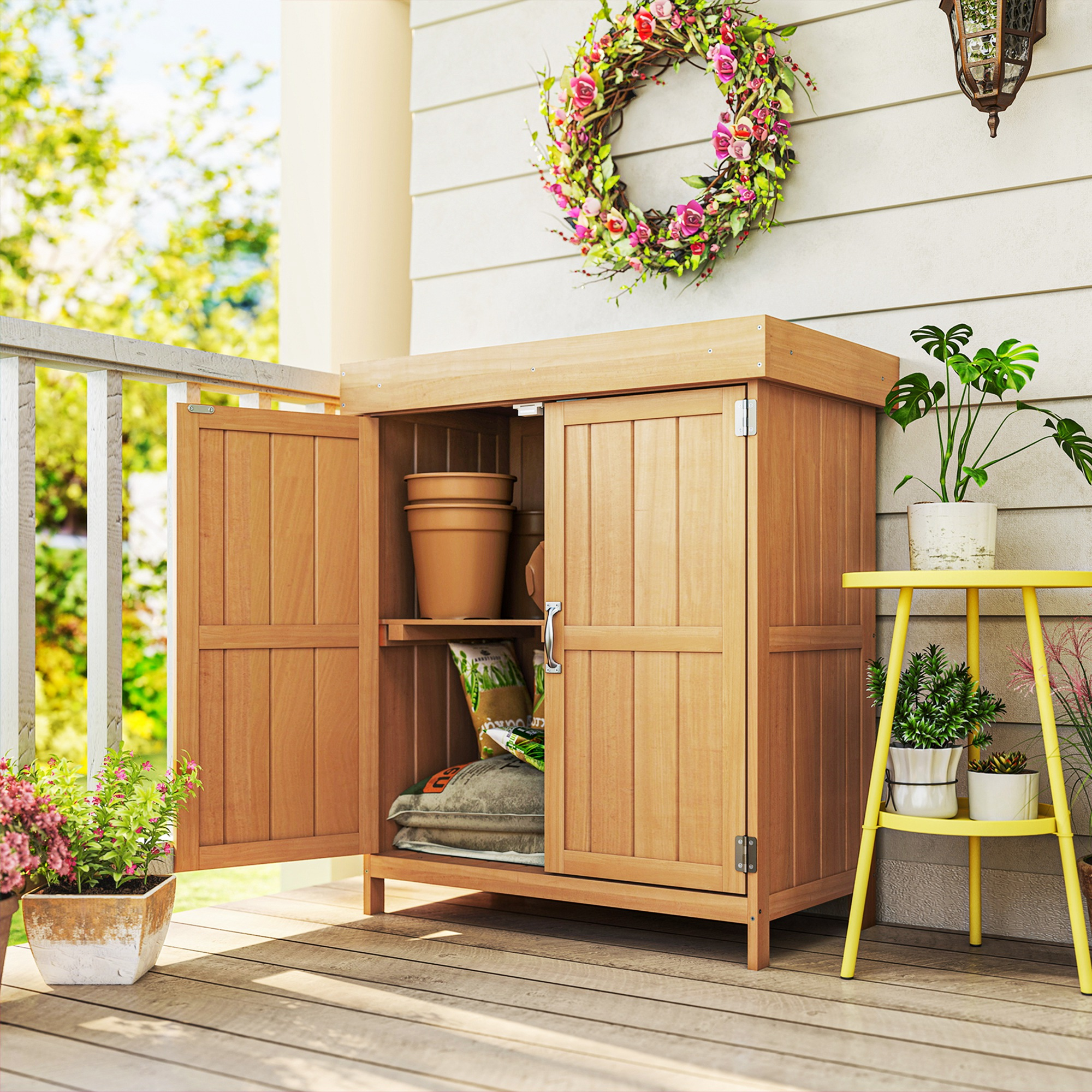 Mobile contenitore in legno su un portico con piante, ghirlanda di fiori e un tavolino giallo con piante.