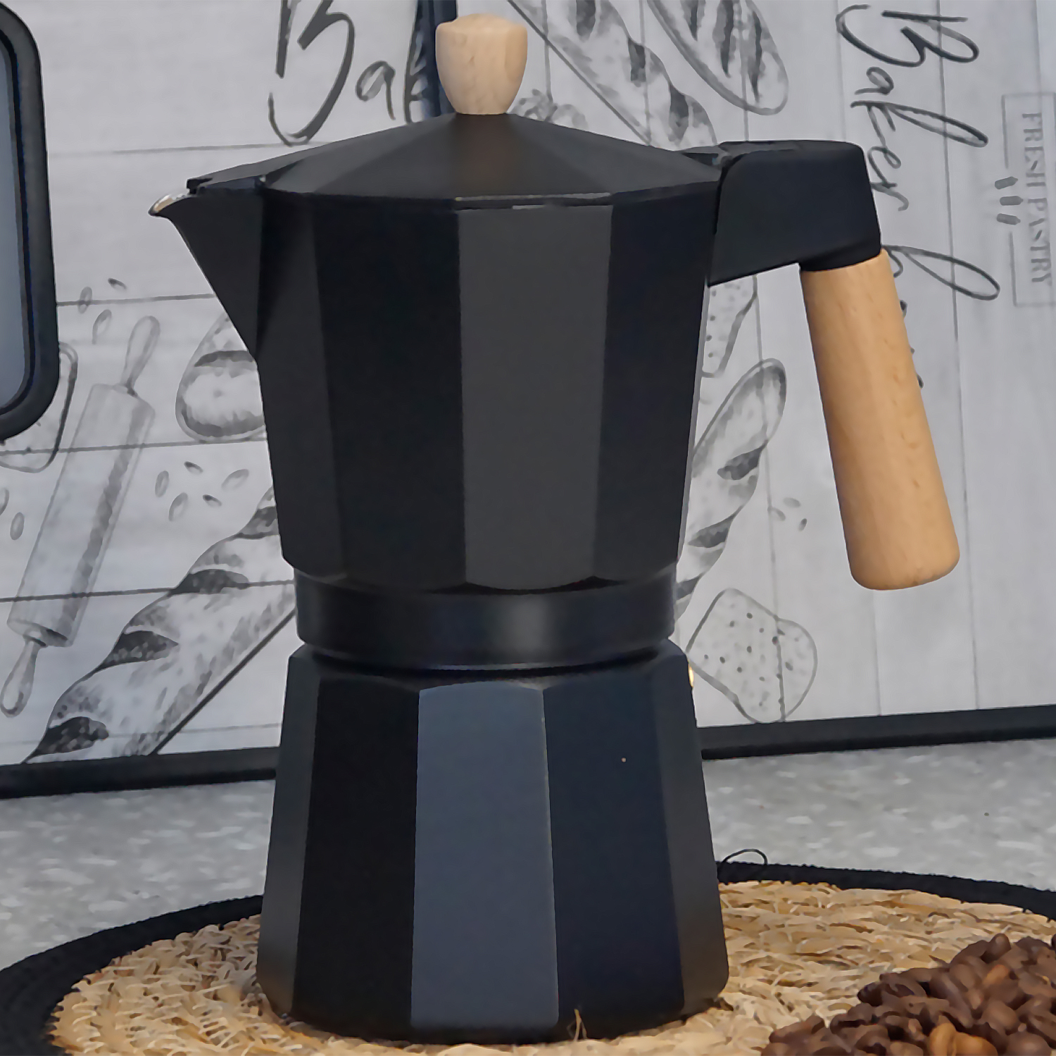 Eine schwarze Mokkakanne mit Holzgriff und -knopf steht auf einer gewebten Matte. Kaffeebohnen sind rechts unten.