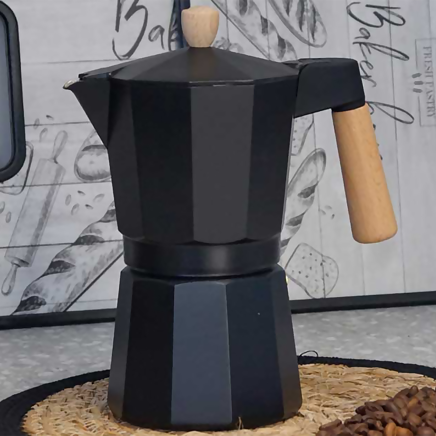 Eine schwarze Mokkakanne mit Holzgriff und -knauf steht auf einer gewebten Matte. Kaffeebohnen sind unten rechts.