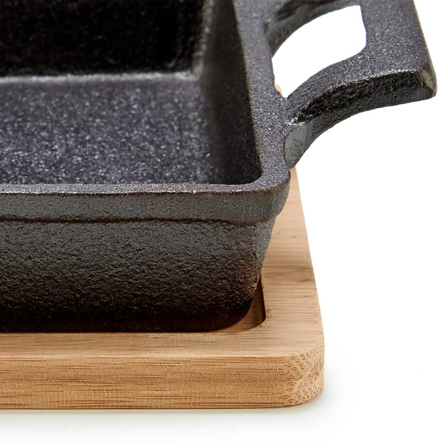 Primer plano de una sartén de hierro fundido negro con asa, sobre un salvamanteles de madera sobre fondo blanco.