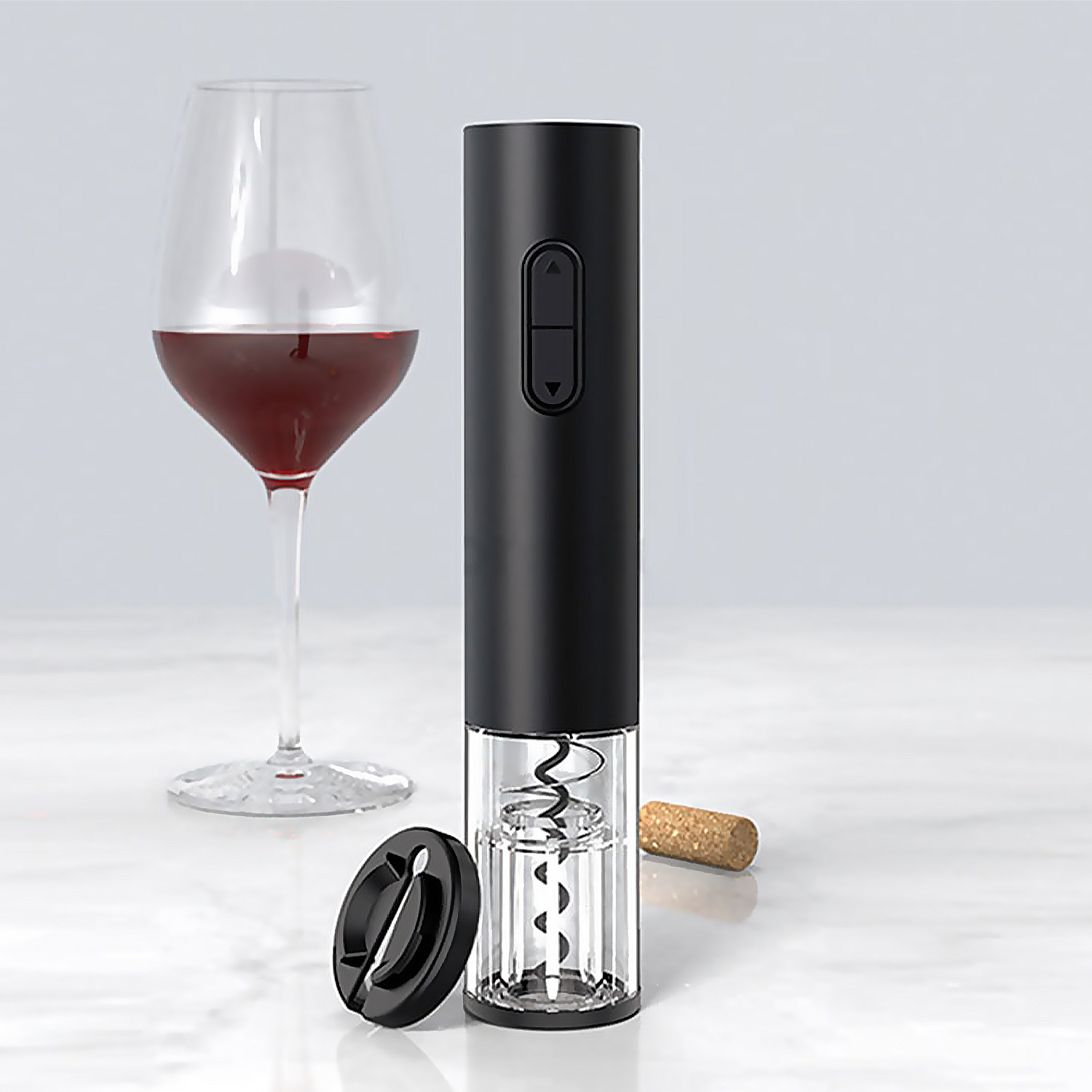 Un bicchiere di vino con vino rosso, un apribottiglie elettrico nero, un tappo e un tagliacapsule nero su una superficie bianca.