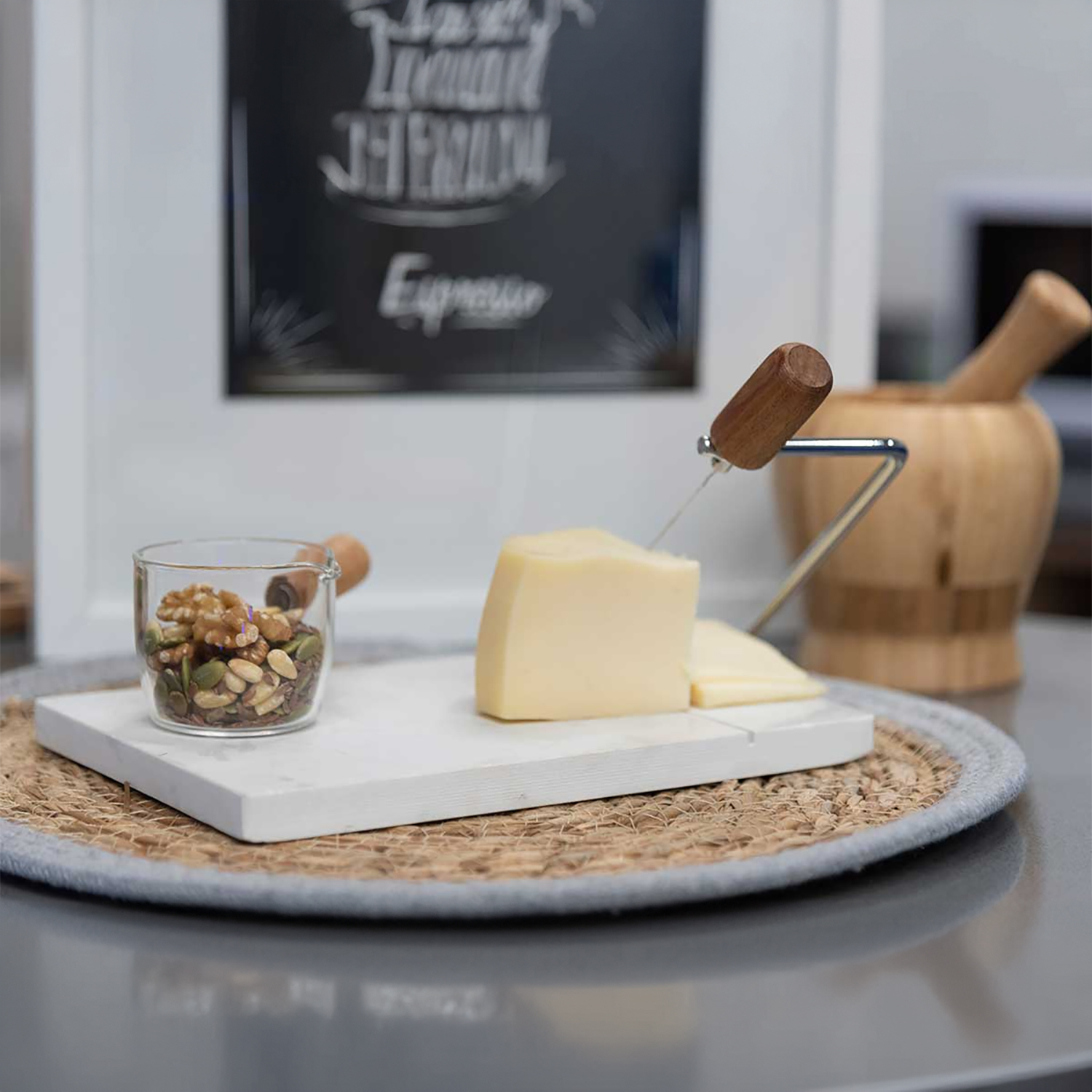 Ein Käsebrett mit Käse, Nüssen und Samen. Ein Käseschneider und ein Mörser sind daneben. Im Hintergrund befindet sich eine Tafel.