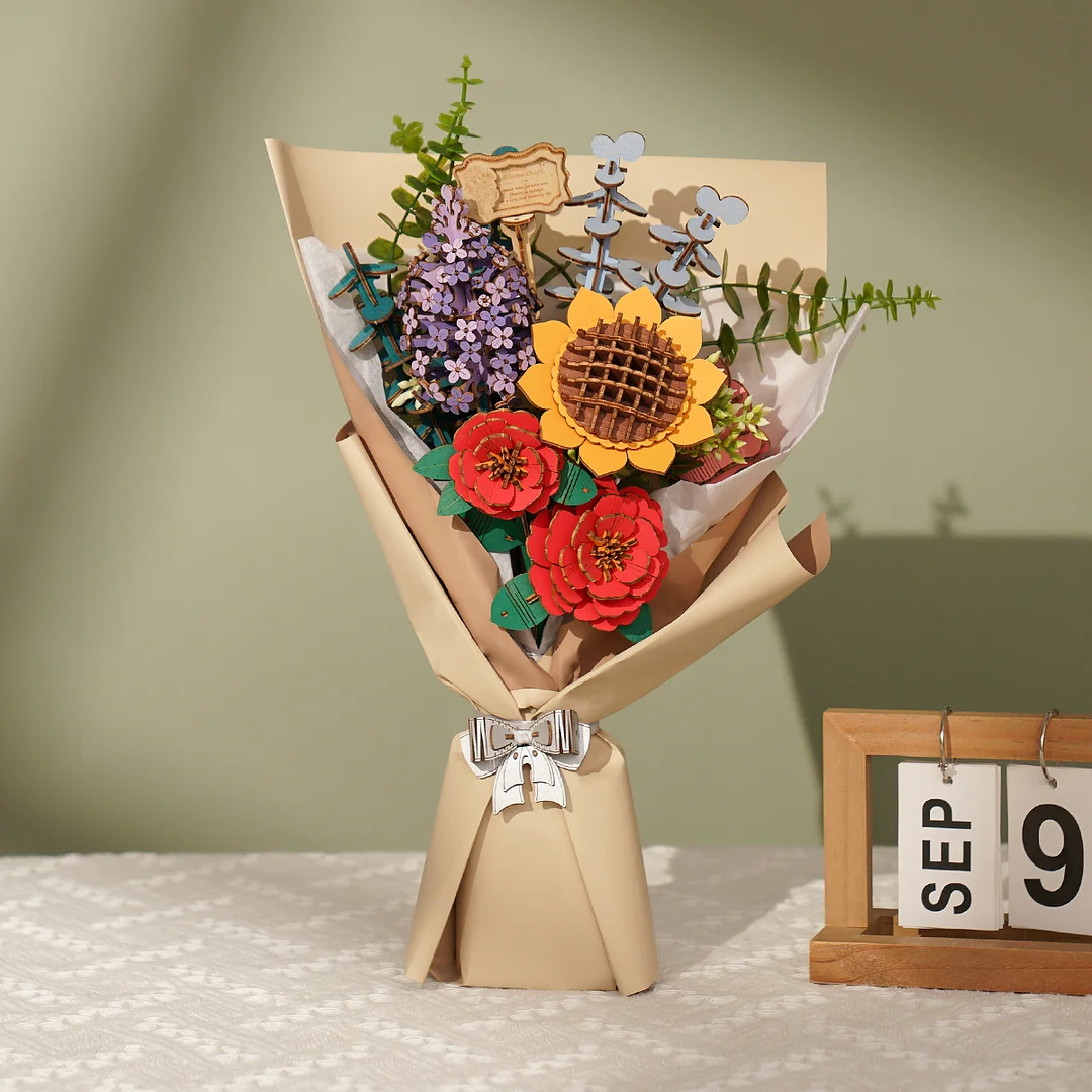Een boeket houten bloemen, waaronder een zonnebloem en rode bloemen, verpakt in papier, met een kalender waarop 9 september staat.