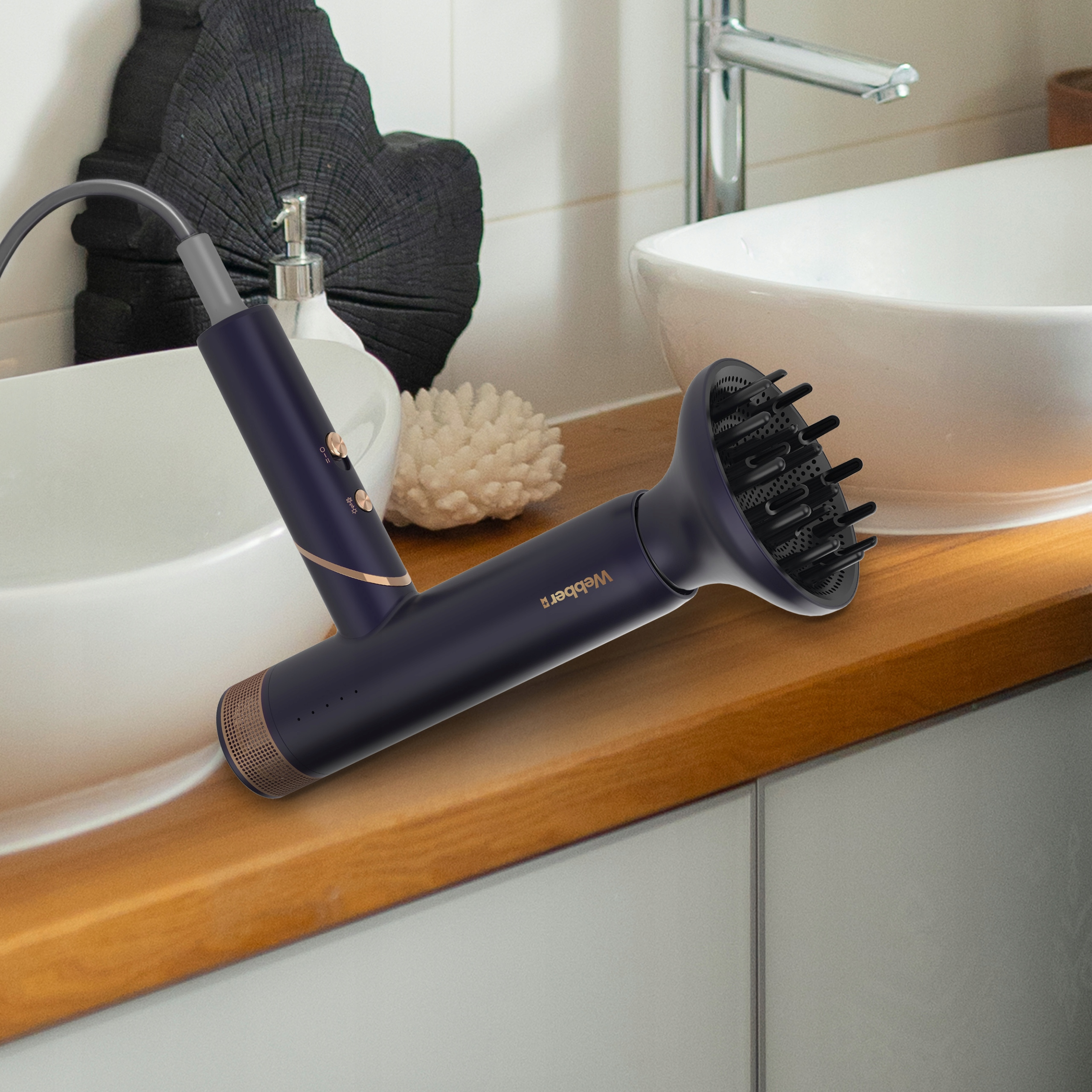 Ciemnoniebieska suszarka do włosów z dyfuzorem leży na drewnianym blacie. Widoczne są dwie białe umywalki i czarny drewniany element dekoracyjny.