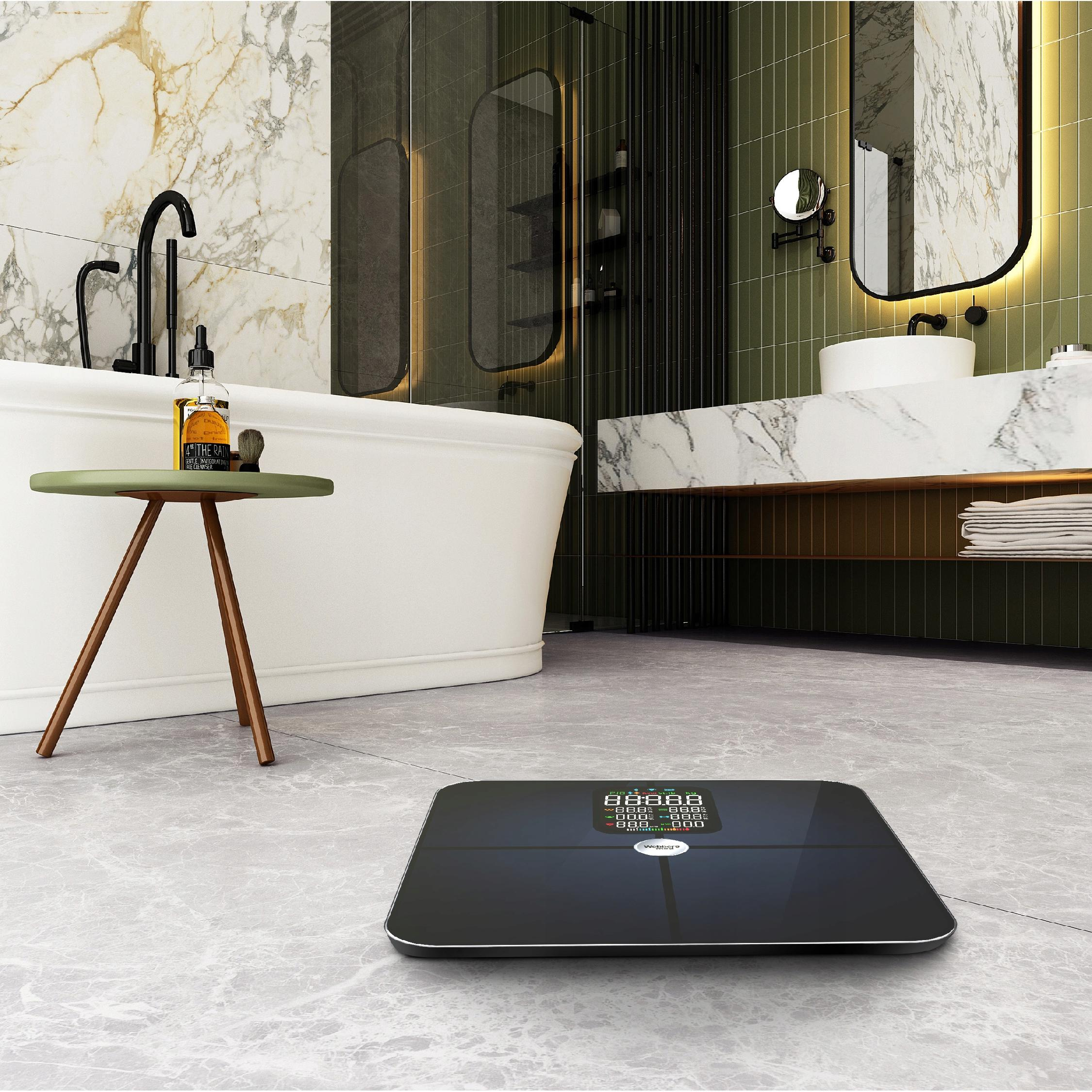 Nowoczesna łazienka z wagą na podłodze. Widoczna wanna, stolik z butelką i lustro.