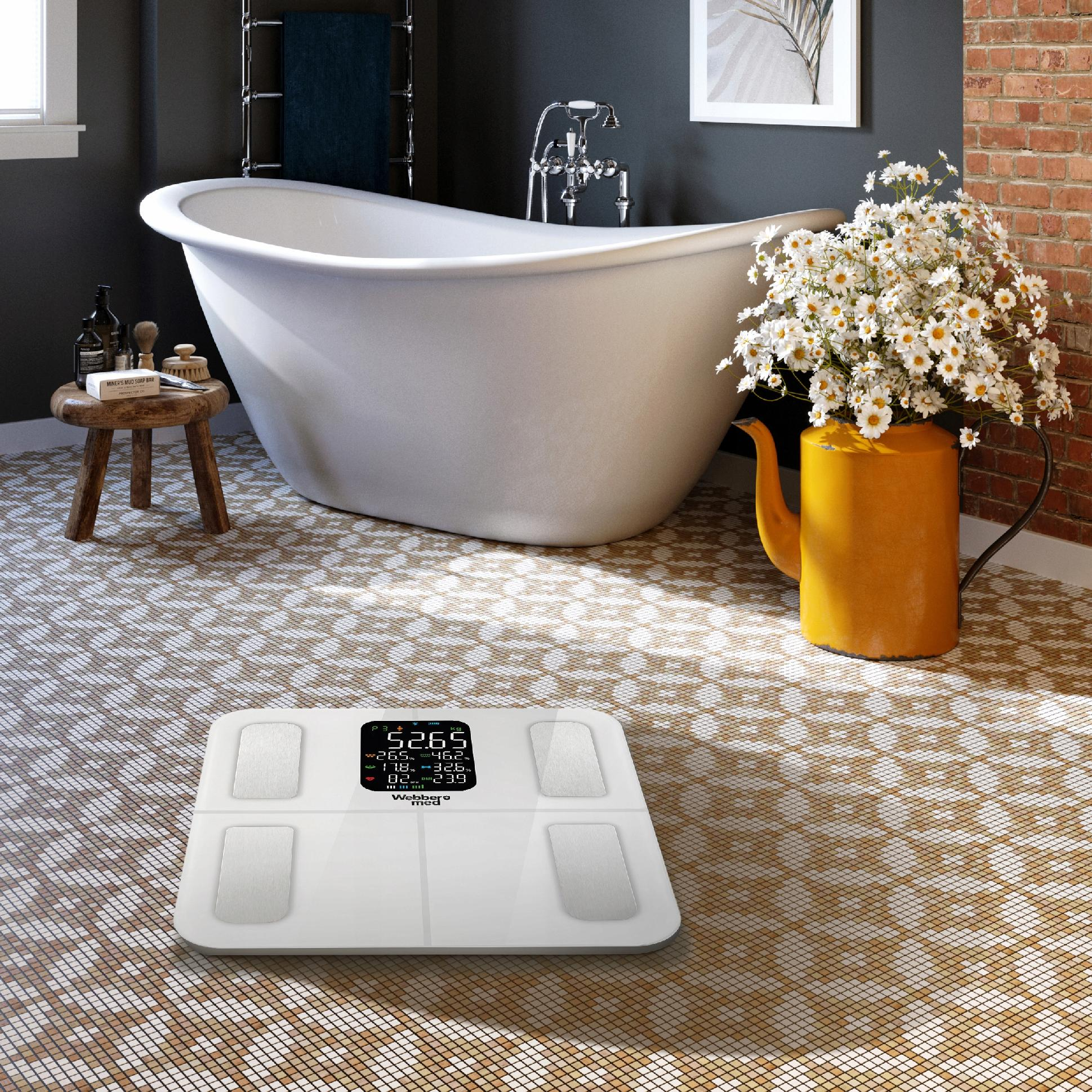 Łazienka z białą wanną, wagą, żółtym dzbanem z kwiatami i stołkiem z kosmetykami. Podłoga z płytek mozaikowych.