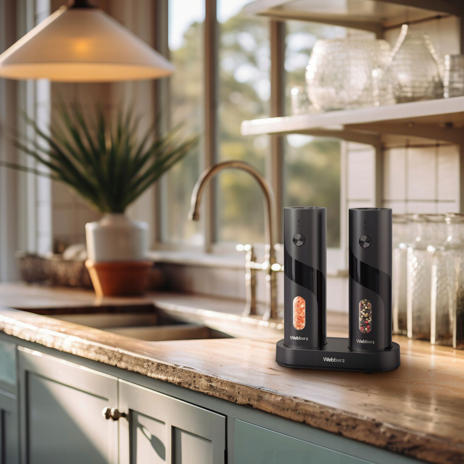 Dwa czarne elektryczne młynki do soli i pieprzu na drewnianym blacie. Zielona roślina i przedmioty kuchenne w tle.