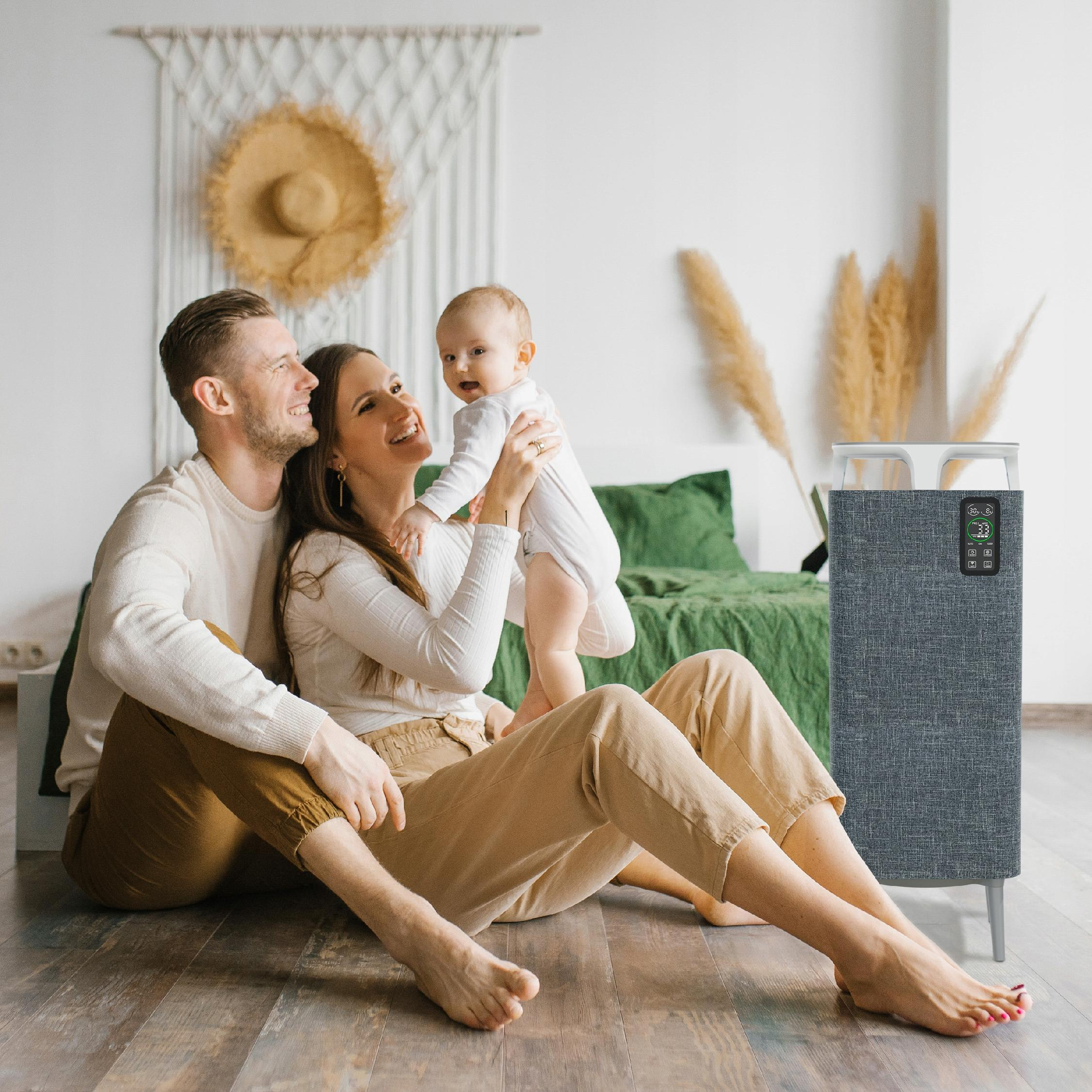 Rodzina siedzi na podłodze z dzieckiem. Obok nich stoi oczyszczacz powietrza. Kapelusz wisi na ścianie.