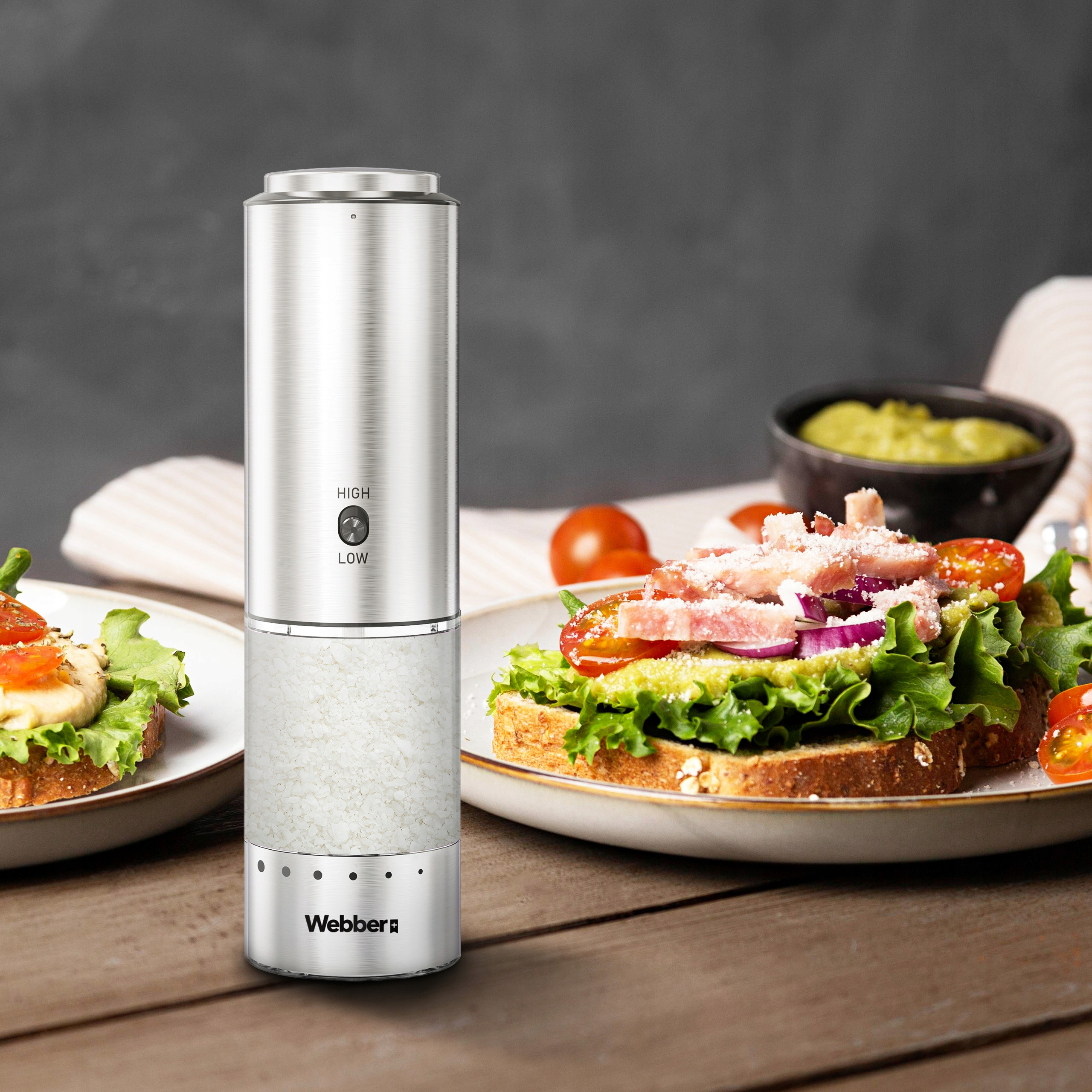 Metalowy młynek do soli obok dwóch kanapek z pomidorami, sałatą i awokado.