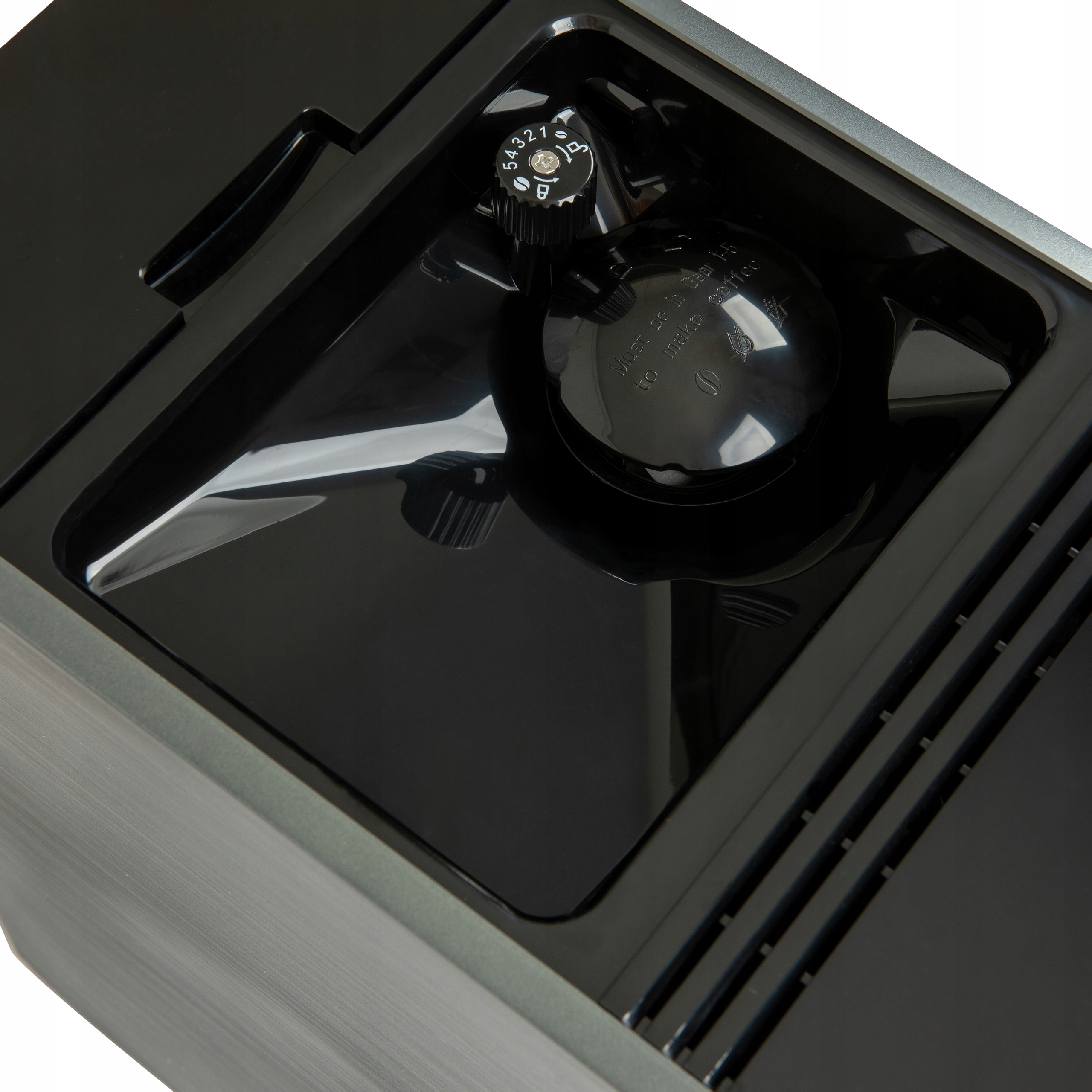 Zbliżenie czarnego elementu ekspresu do kawy z pokrętłem, błyszczącymi powierzchniami i metalową szarą ramą.