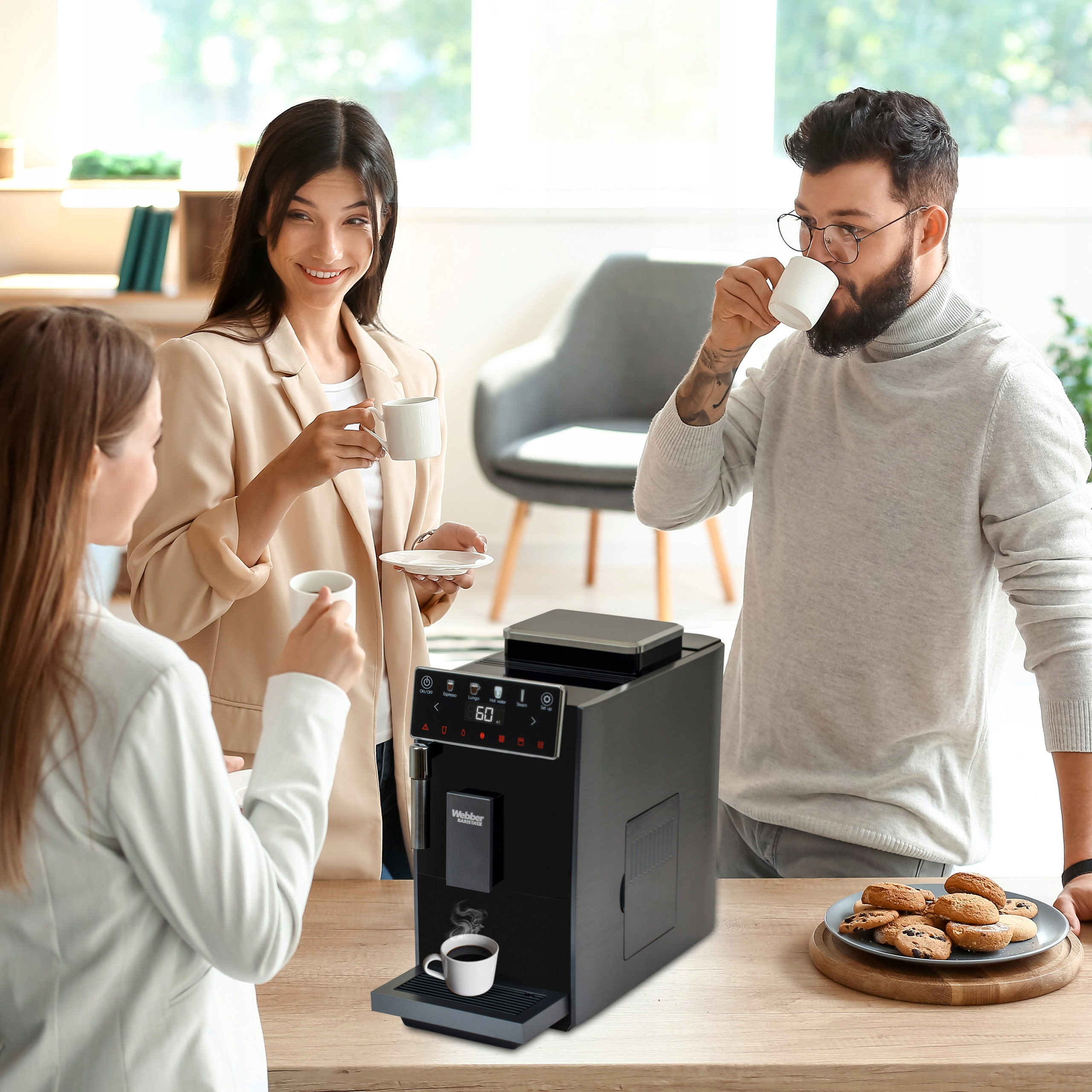 Trzy osoby piją kawę w pobliżu ekspresu do kawy. Ciastka na stole. Okno w tle.