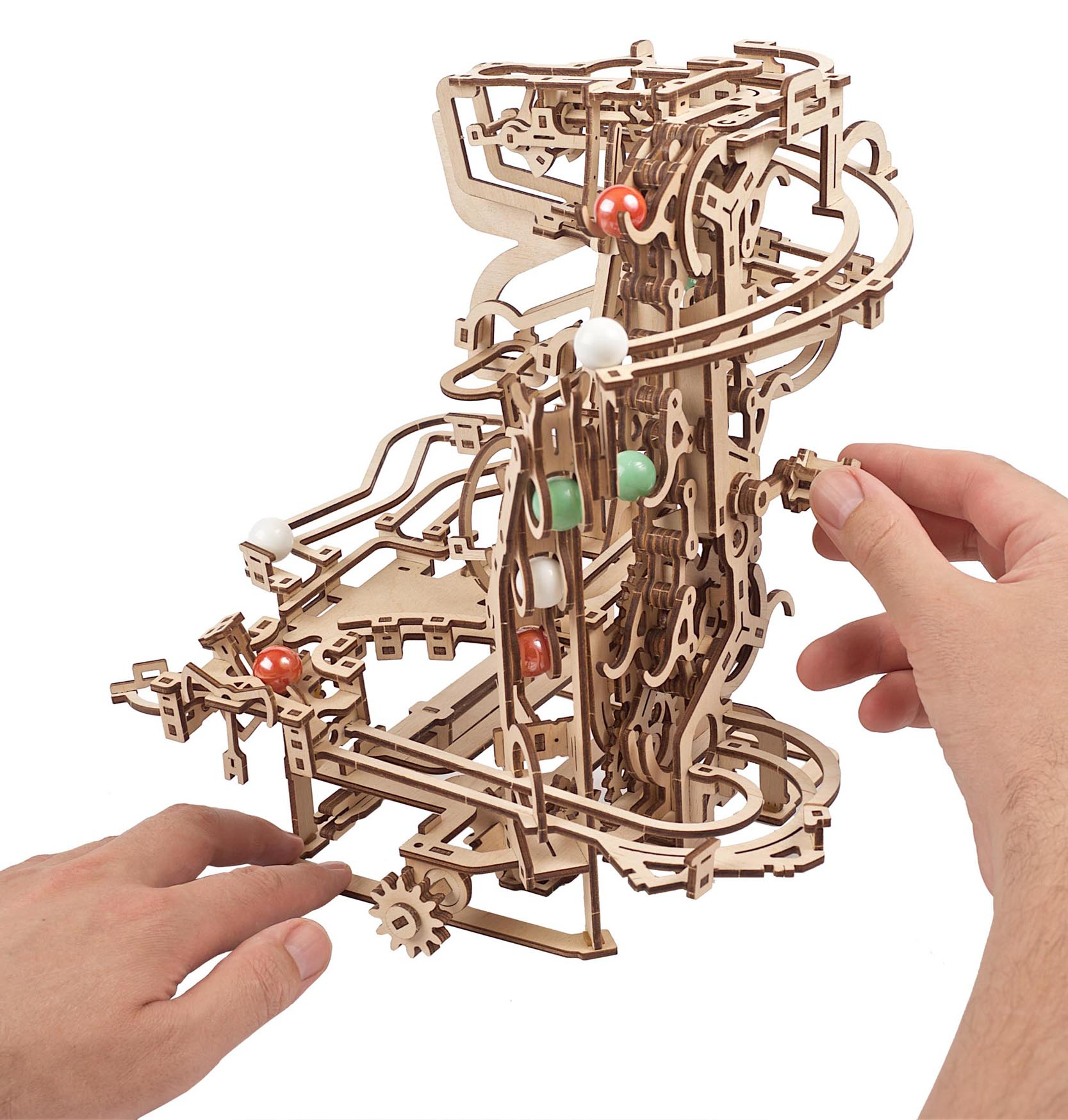 Drewniany tor kulkowy z czerwonymi, białymi i zielonymi kulkami. Dłonie montują konstrukcję.