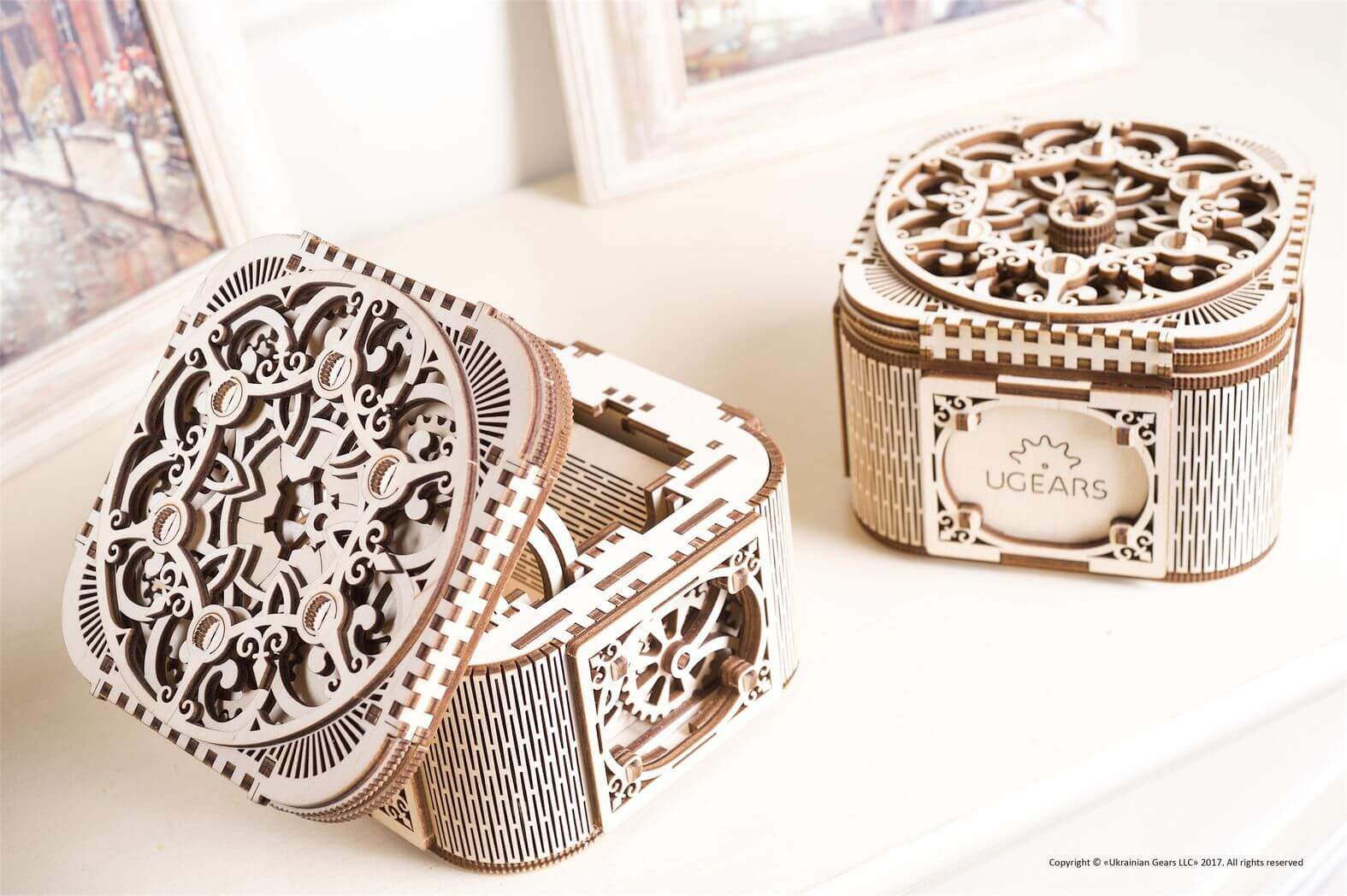 Dwa skomplikowane drewniane pudełka z puzzlami na białej powierzchni. Jedno otwarte, odsłaniające wewnętrzne koła zębate; drugie zamknięte.