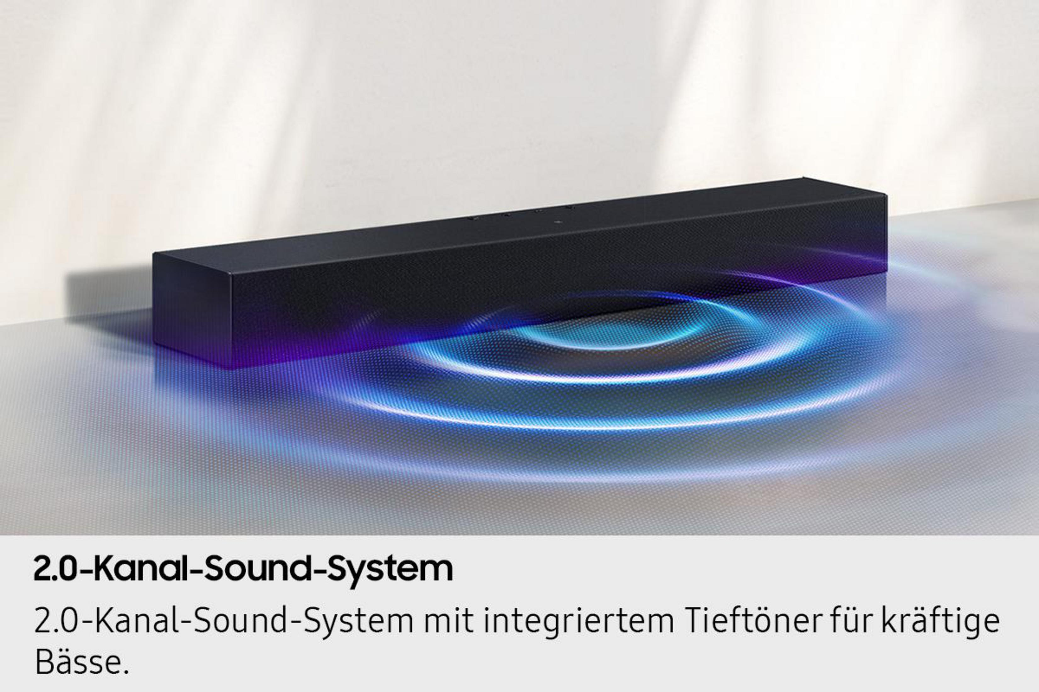 Czarny soundbar z efektem niebieskiej fali dźwiękowej na teksturowanej powierzchni. Biała ściana w tle.
