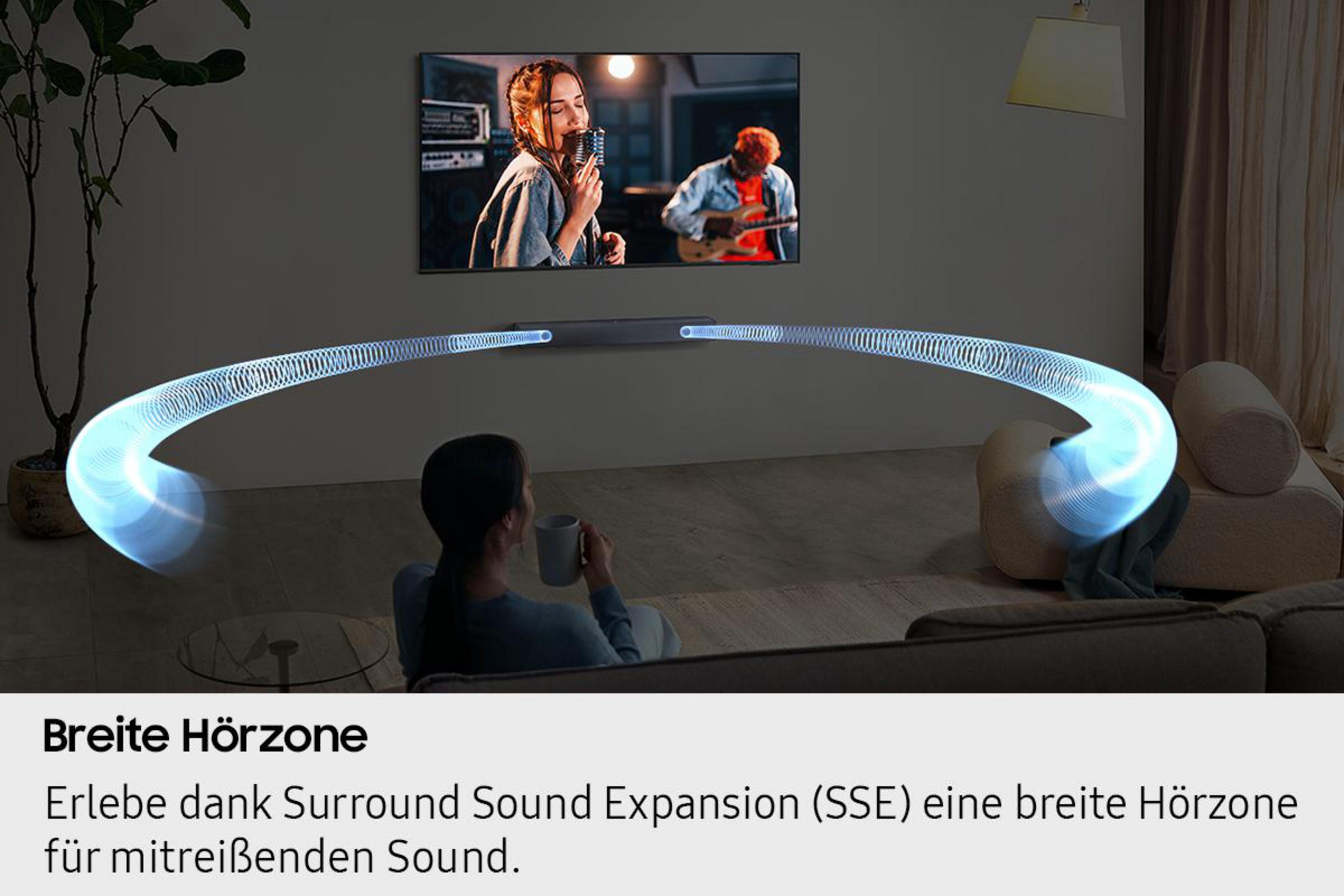 Kobieta ogląda TV z piosenkarką na scenie, soundbarem, świecącym łukiem i kobietą z kubkiem.