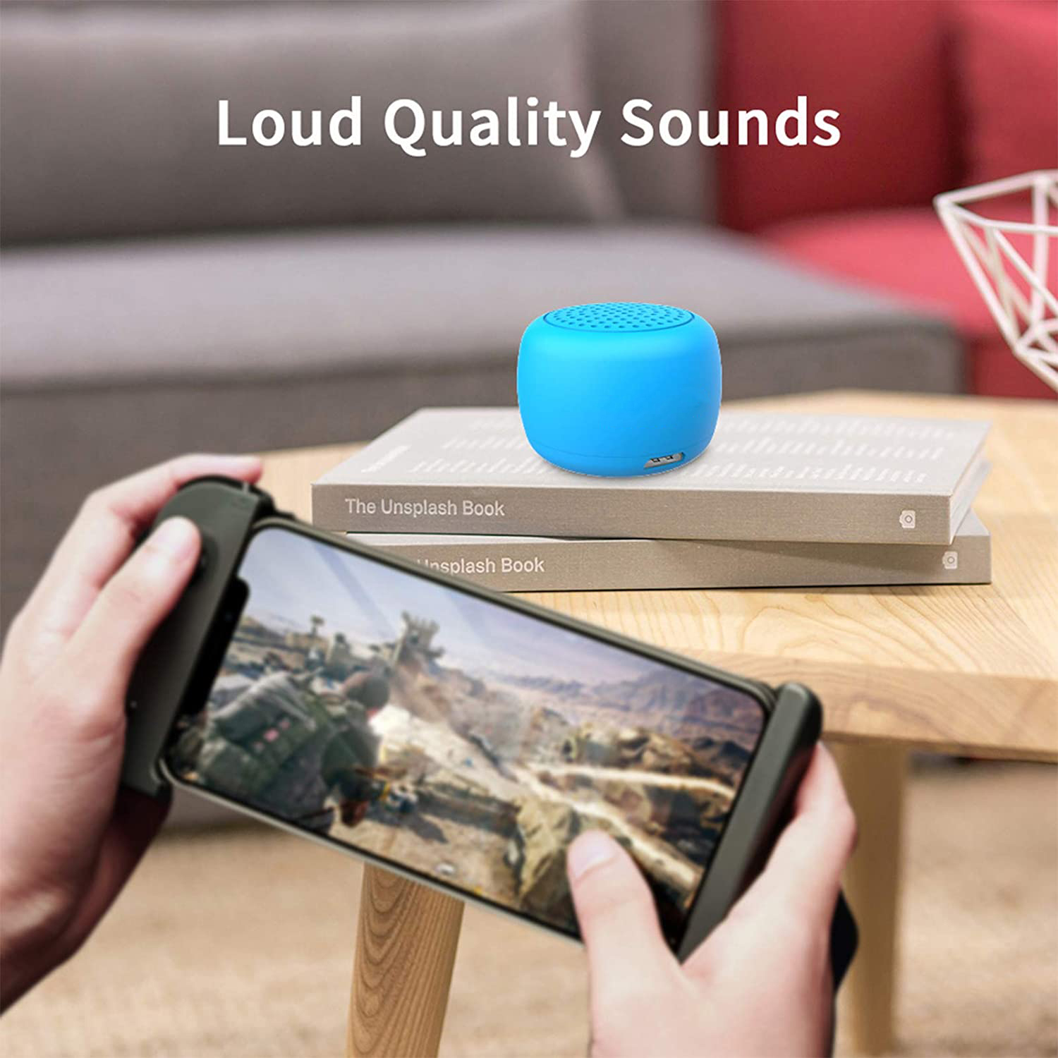 Eine Person hält ein Telefon mit Controller. Ein blauer Lautsprecher liegt auf Büchern. Der Text 'Loud Quality Sounds' steht oben.