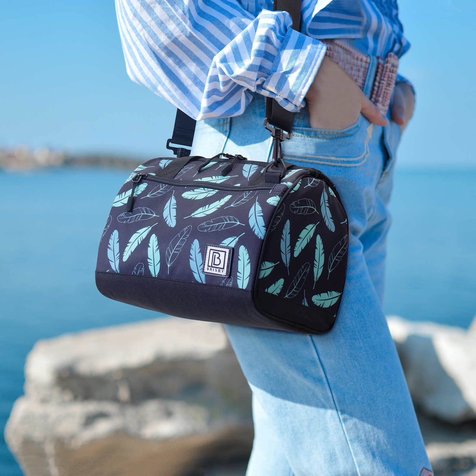 Een persoon met een tas. De tas is zwart met blauwgroene veren. De persoon draagt een spijkerbroek en een blauw gestreept overhemd.