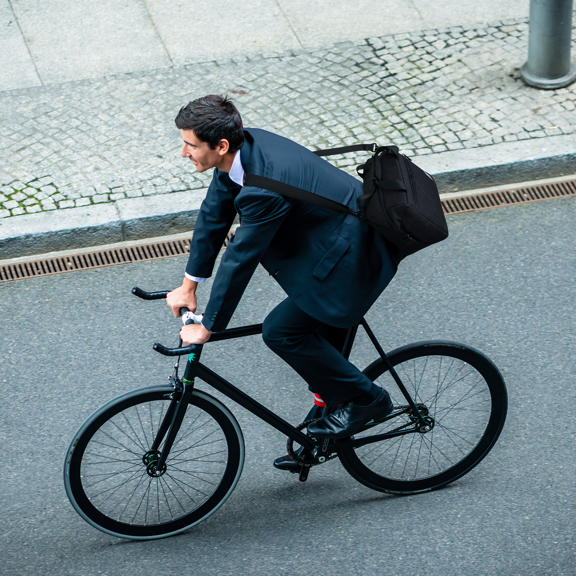 Een man in pak rijdt op een zwarte fiets op straat. Hij heeft een tas op zijn schouder.
