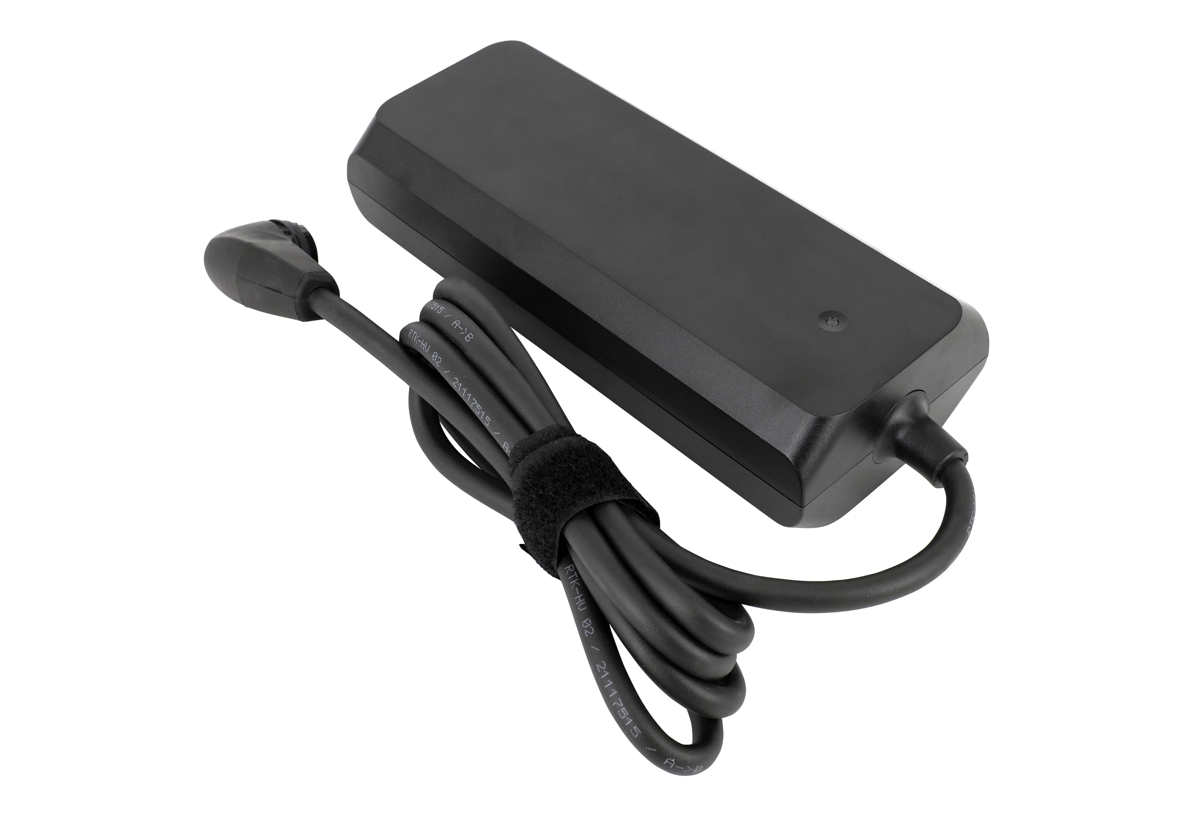 Ein schwarzes Netzteil mit Kabel, das Kabel ist mit Klettverschluss umwickelt. Isoliert auf weißem Hintergrund.