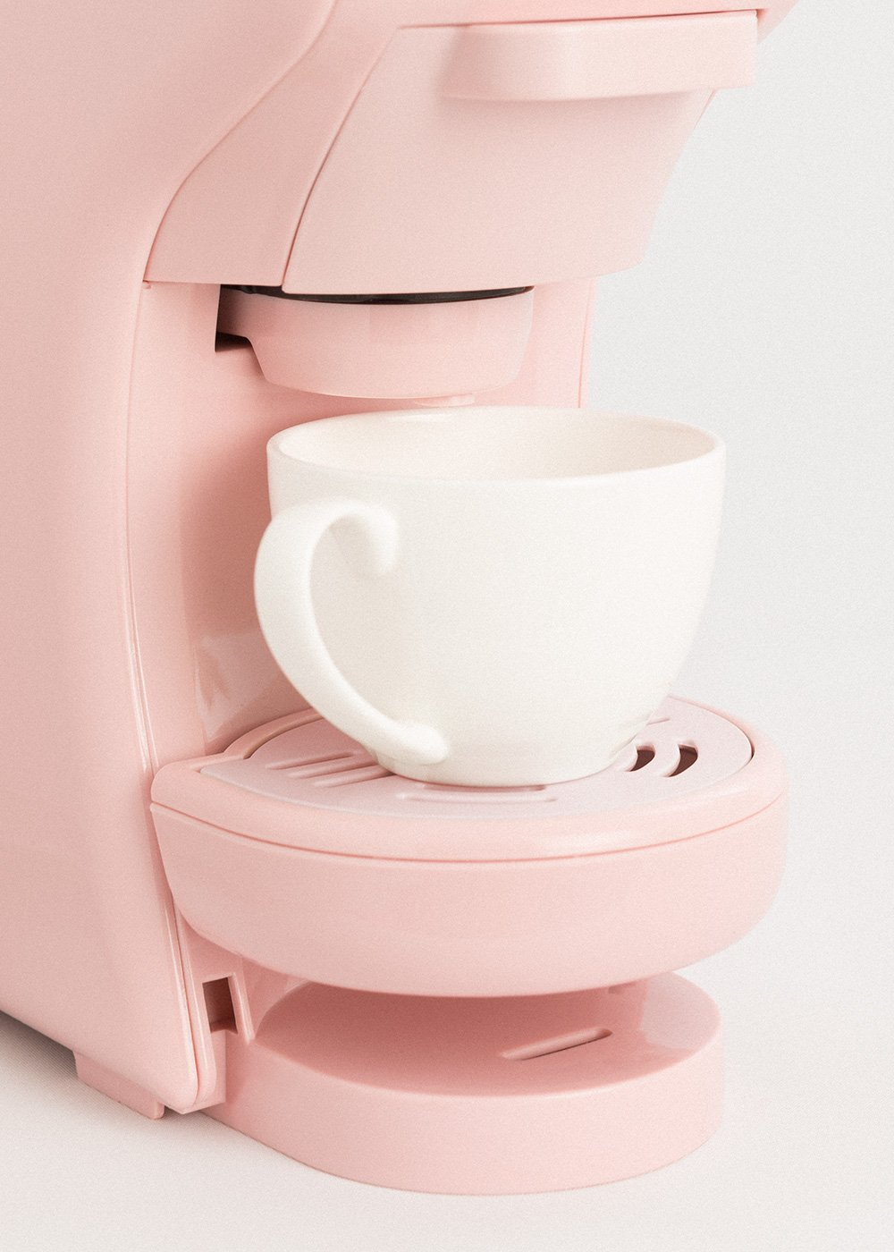 Una cafetera rosa con una taza blanca. La taza está sobre una bandeja. El fondo es blanco.