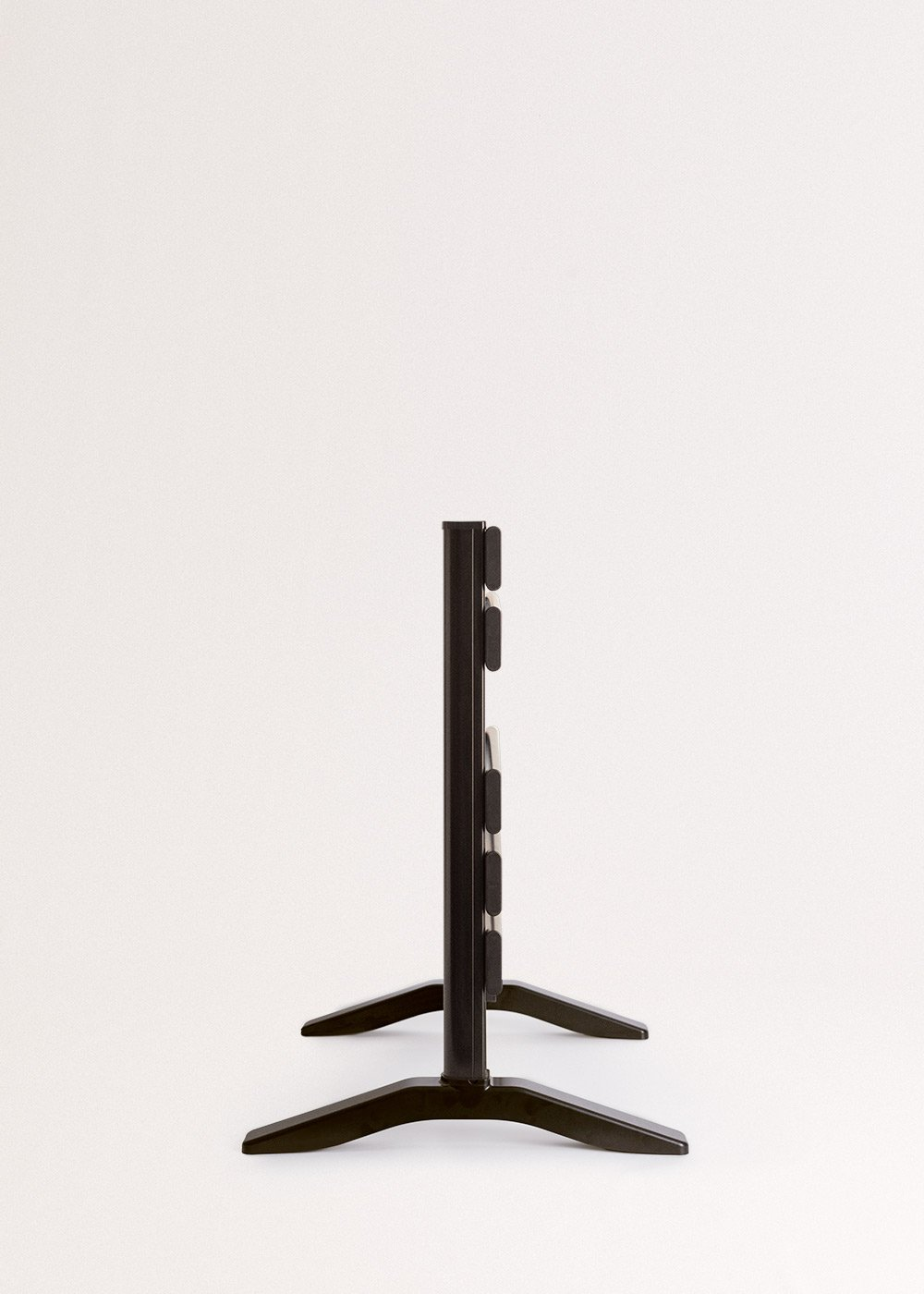 Soporte de TV negro sobre fondo blanco. El soporte tiene un poste vertical con soportes horizontales. Las patas se extienden hacia afuera.