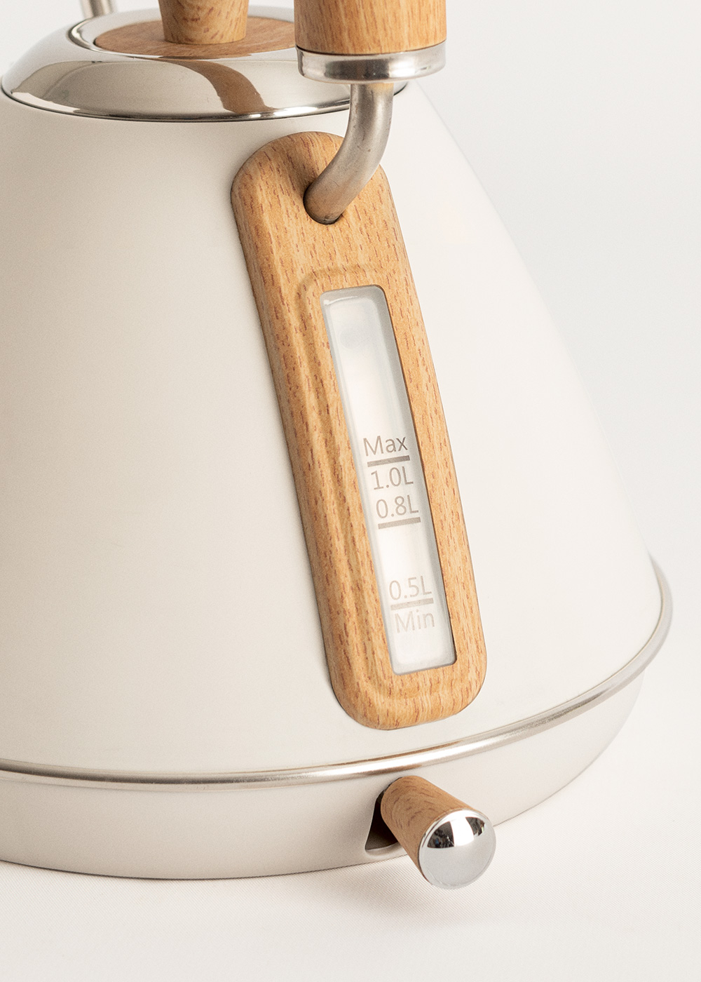 Una tetera crema con detalles de madera. Tiene un indicador de nivel de agua, un asa de madera y un pomo de madera. El fondo es blanco.