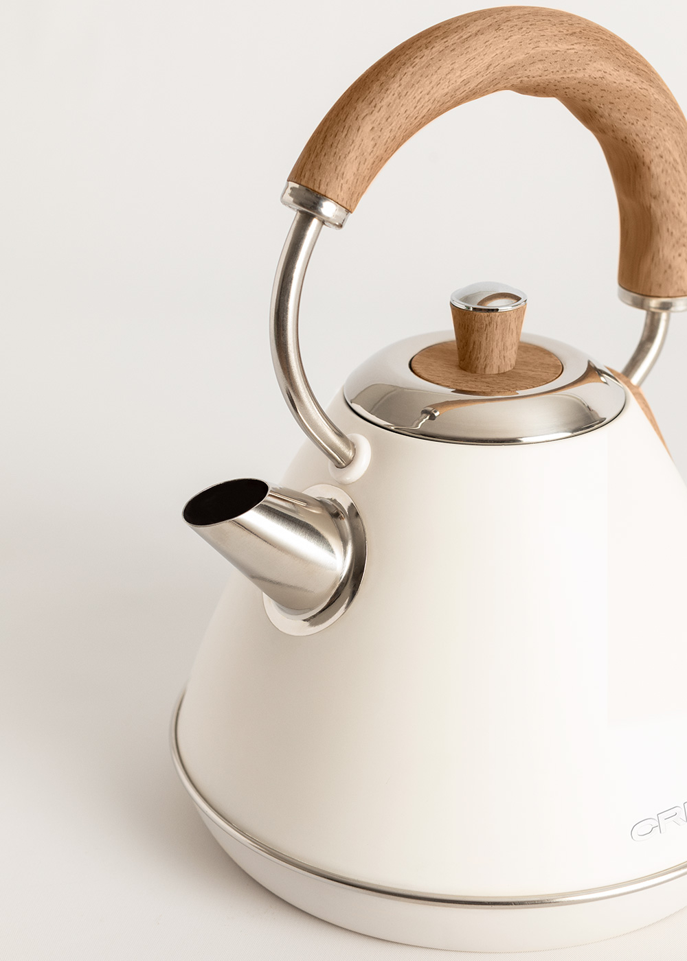 Tetera crema con asa y tapa de madera. Boquilla y base de acero. Fondo blanco. Primer plano.